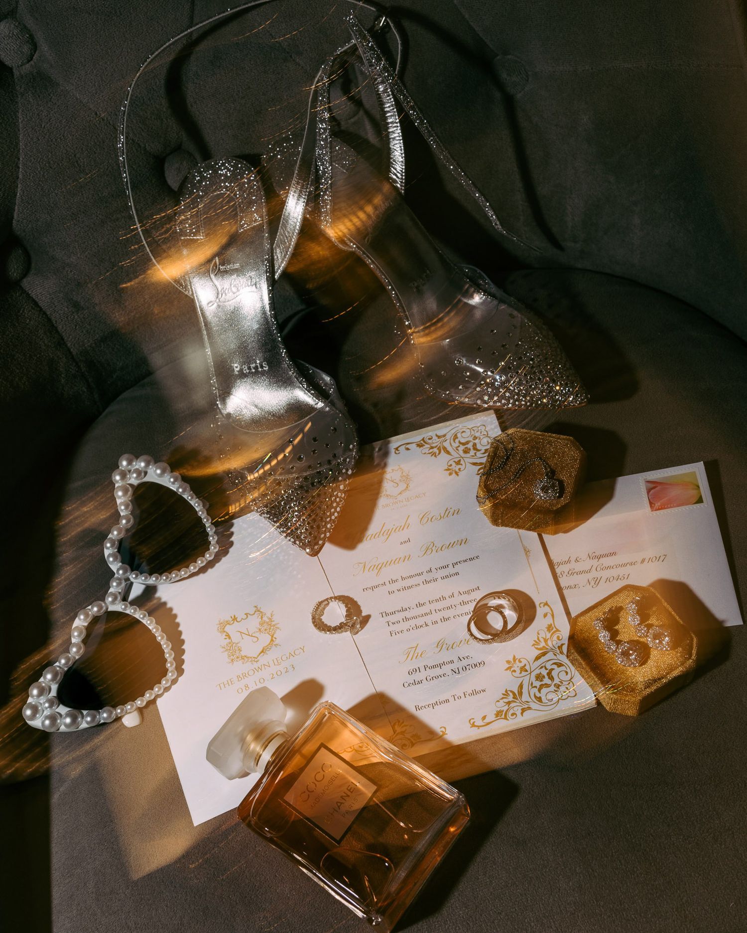 Elegant wedding accessories including sparkly heels, invitation cards and perfume bottle arranged in moody lighting.