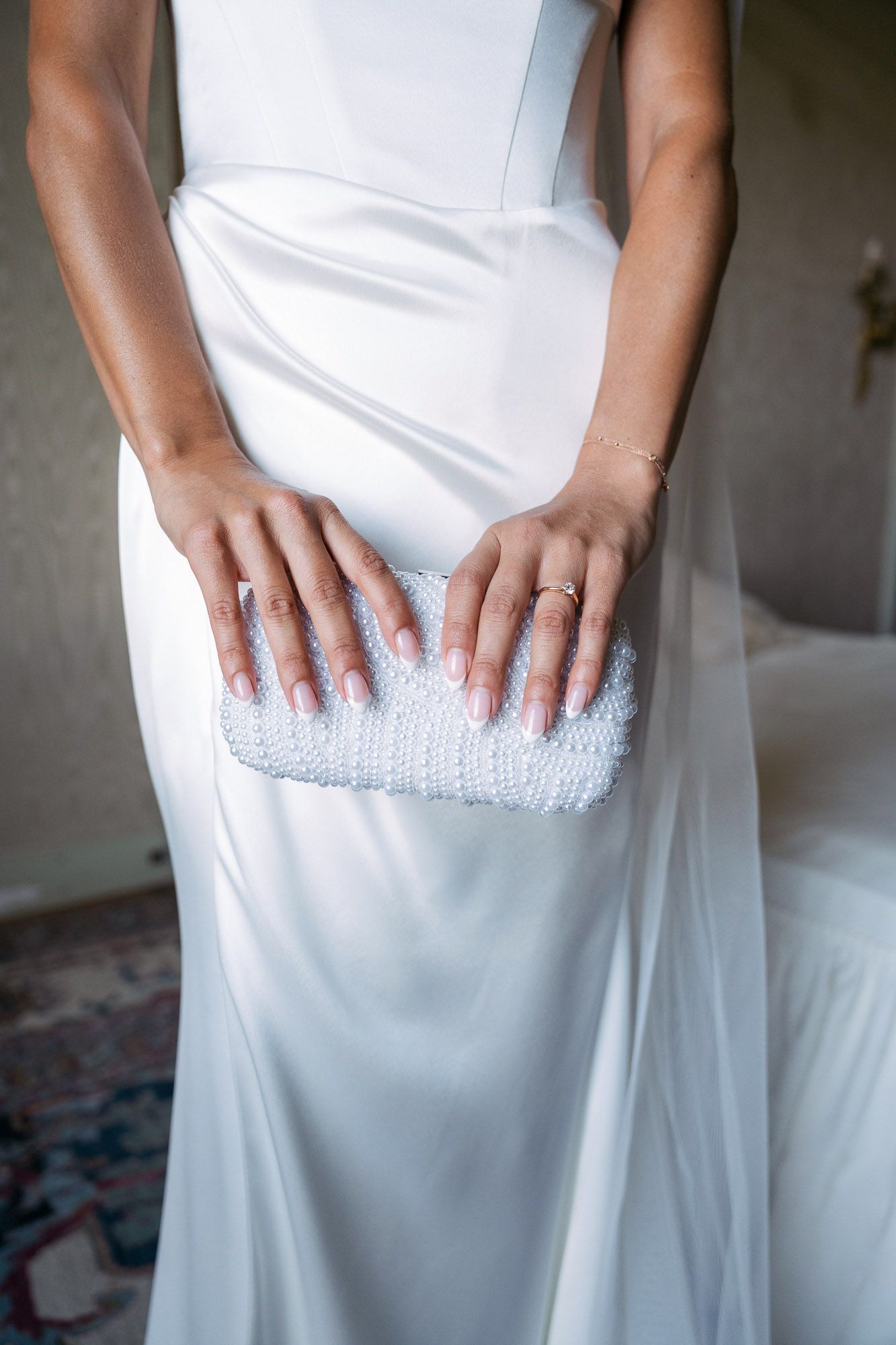 Elegant white bridal clutch purse with beaded details held against flowing wedding dress.