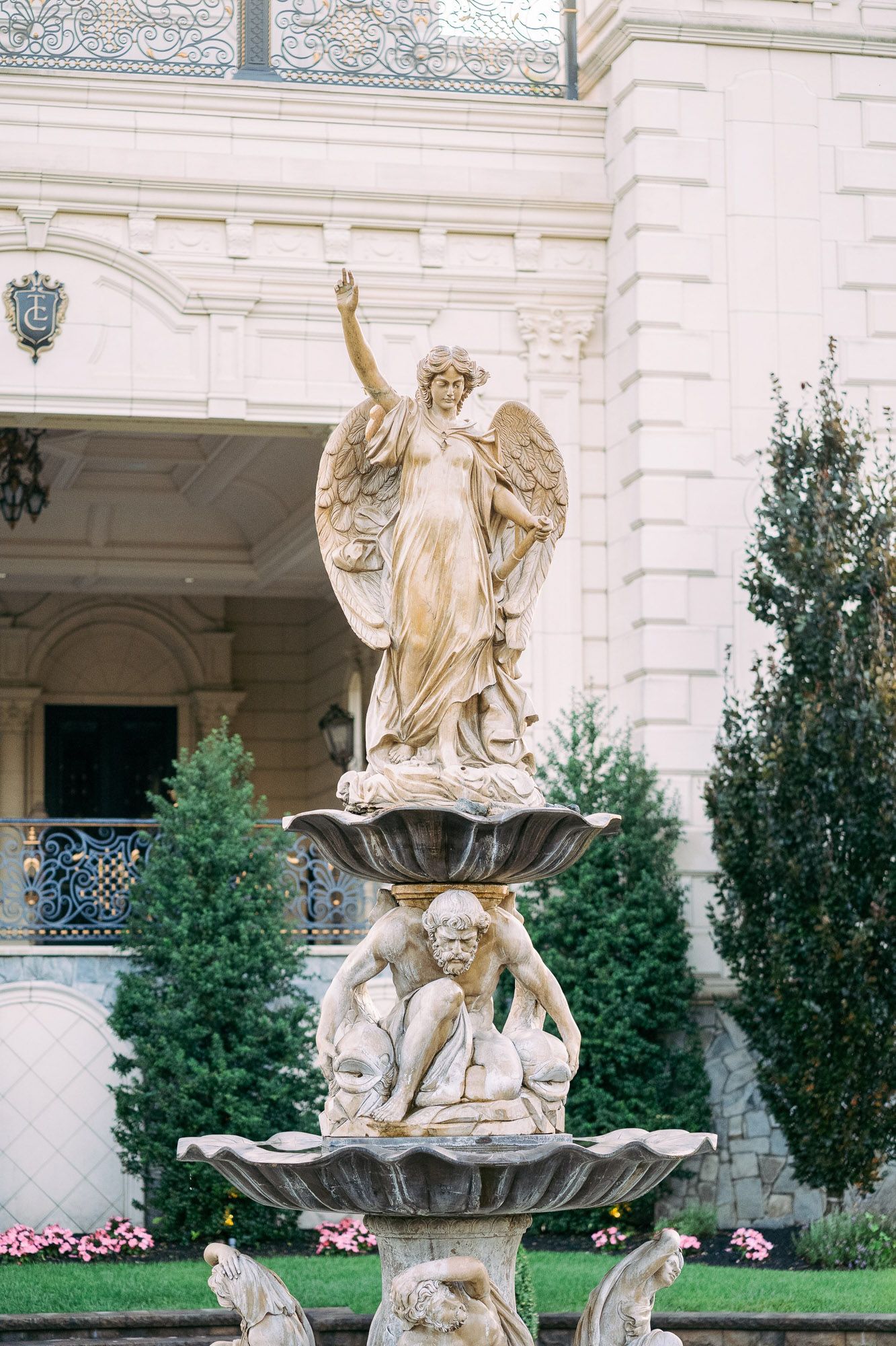 Ornate classical statues and sculptures adorn the exterior of an elegant white stone building with manicured landscaping.