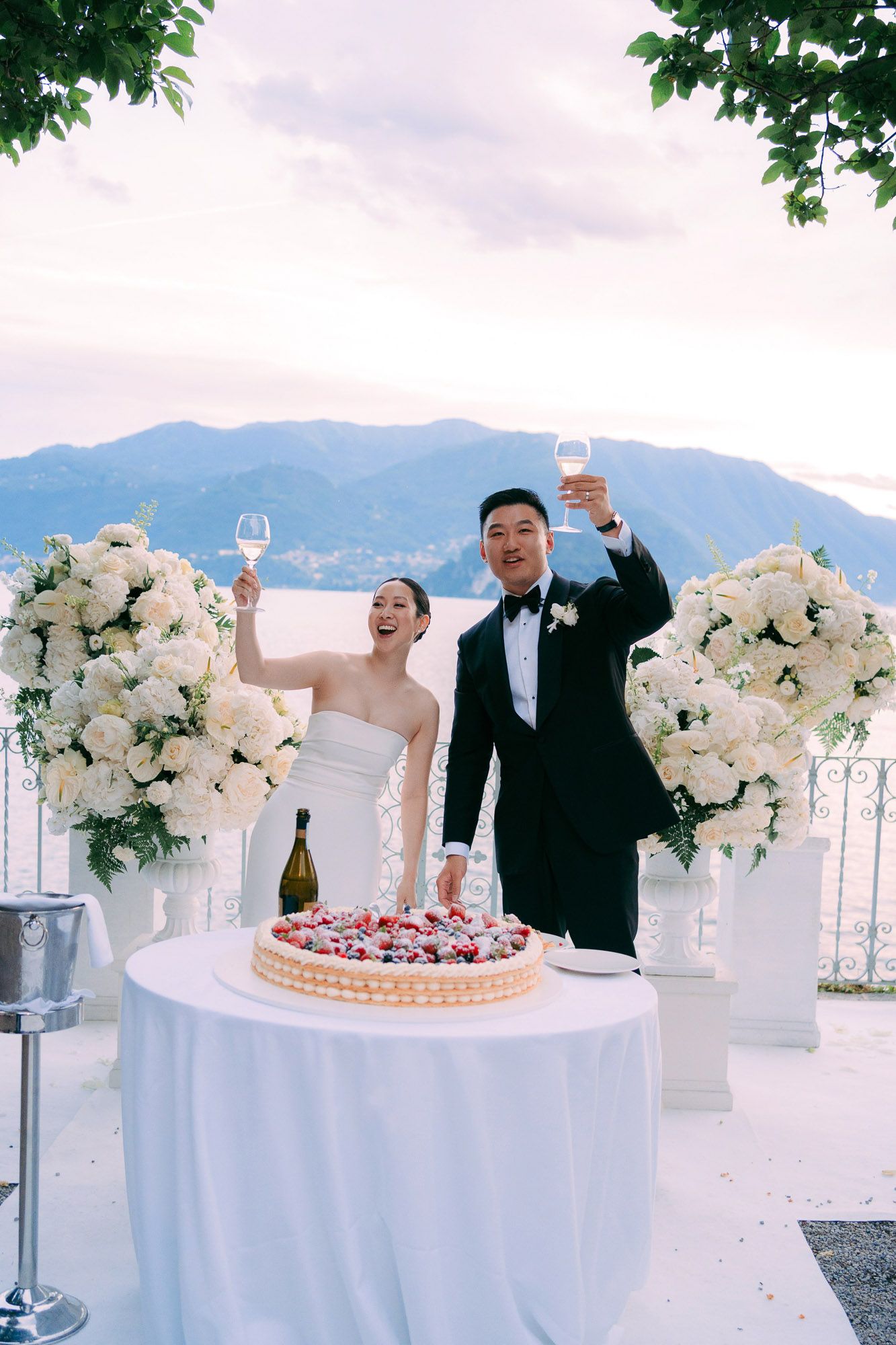 A wedding celebration scene with a cake cutting moment and floral arrangements against a scenic mountain backdrop.