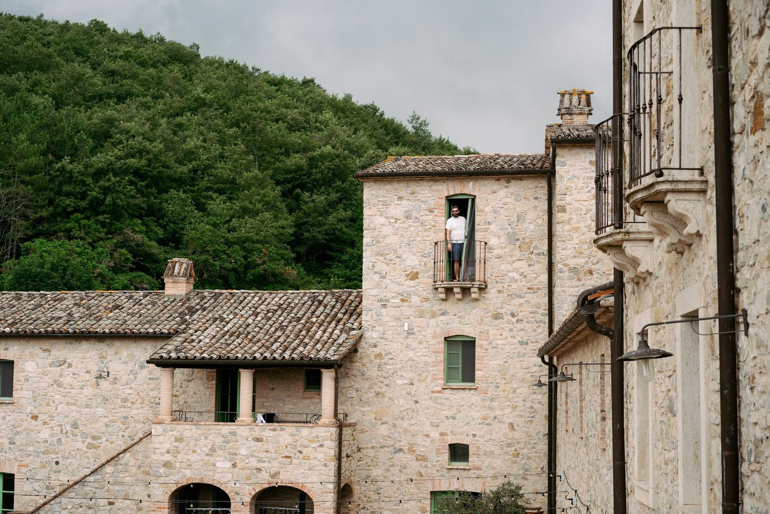 Ancient stone buildings with rustic architecture nestled against green hillside in an Italian countryside setting.