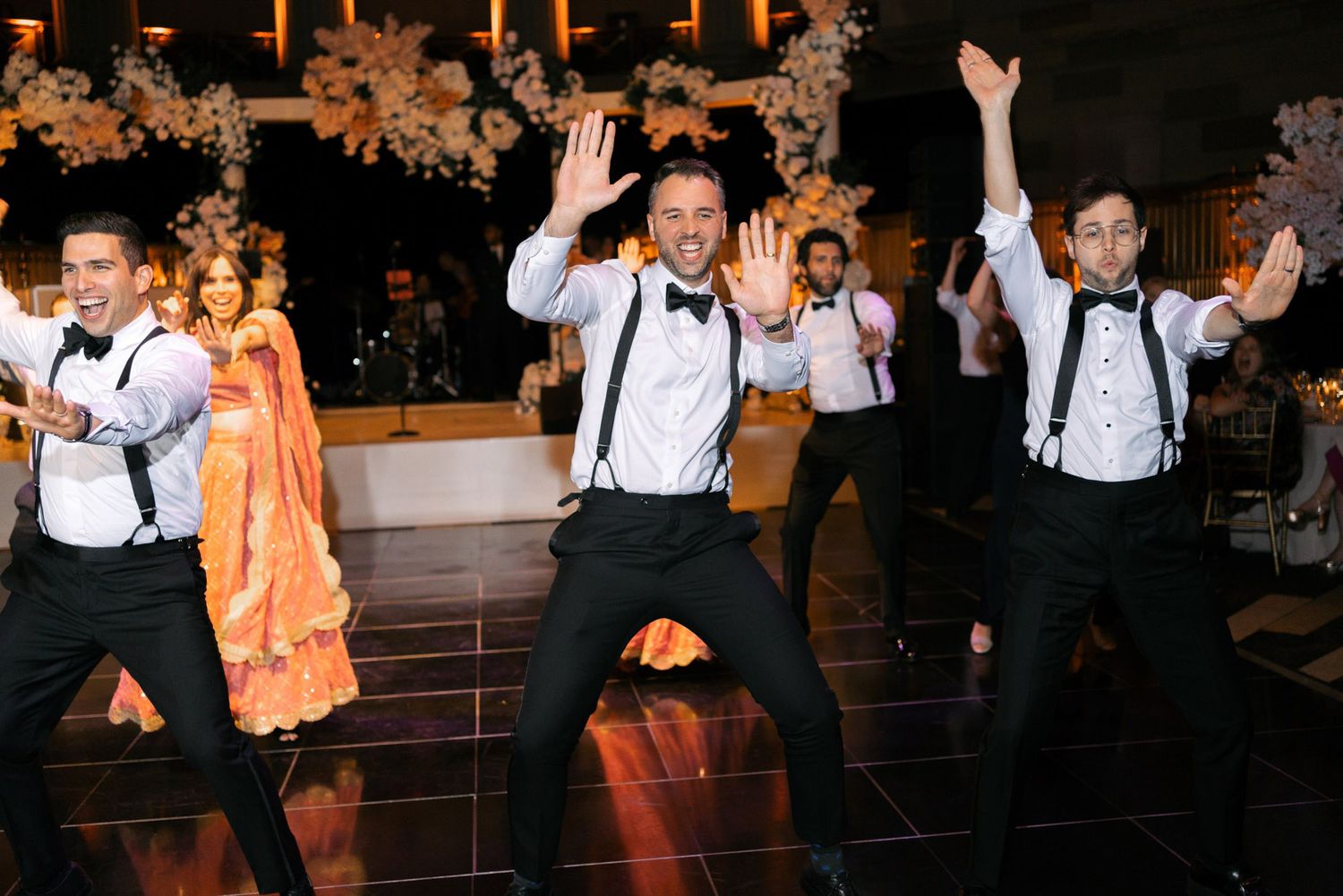 Wedding guests dance and celebrate on a dark dance floor with festive lighting during an evening reception.