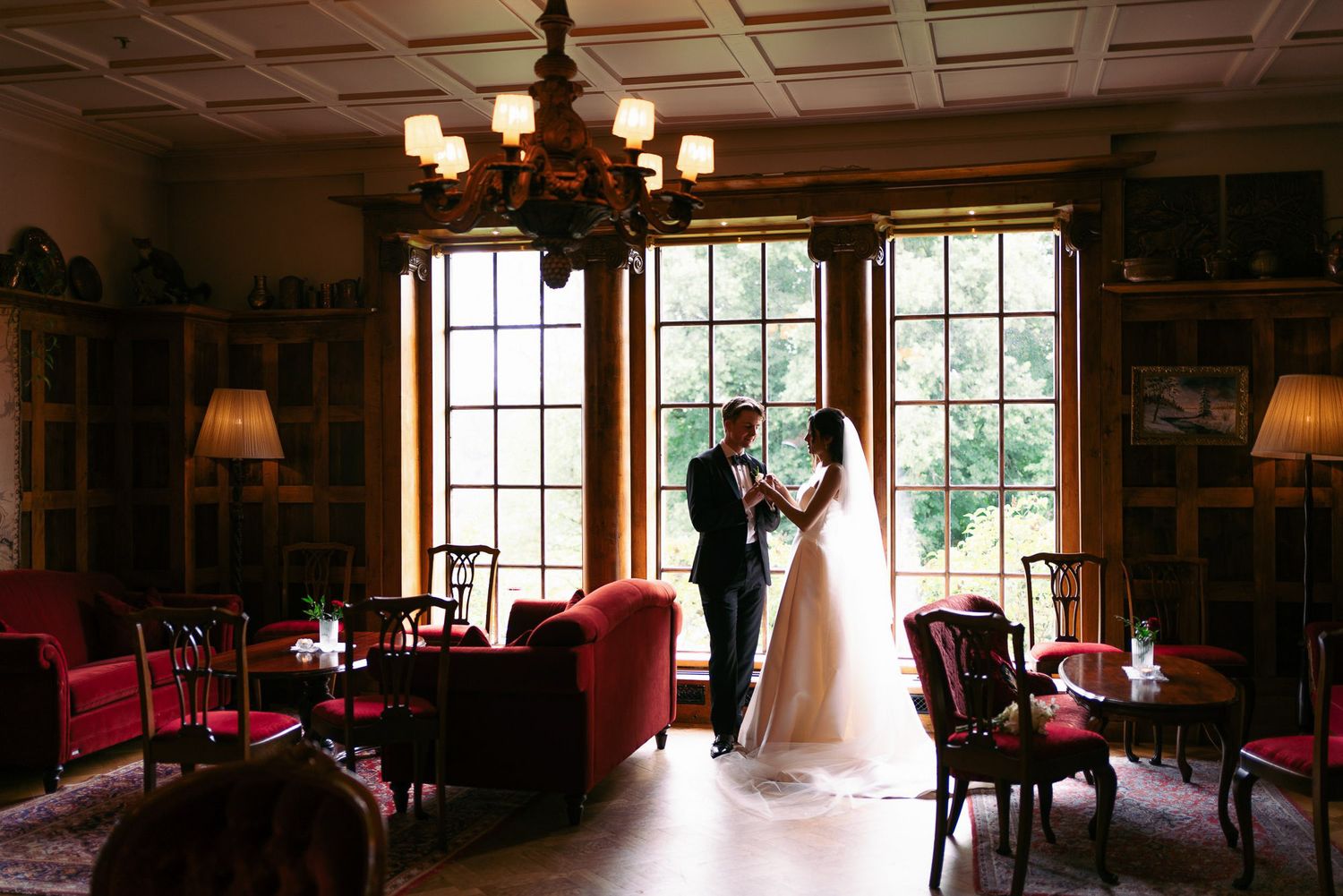 A romantic silhouette in a grand vintage library with red chairs and tall windows, creating an elegant atmosphere.