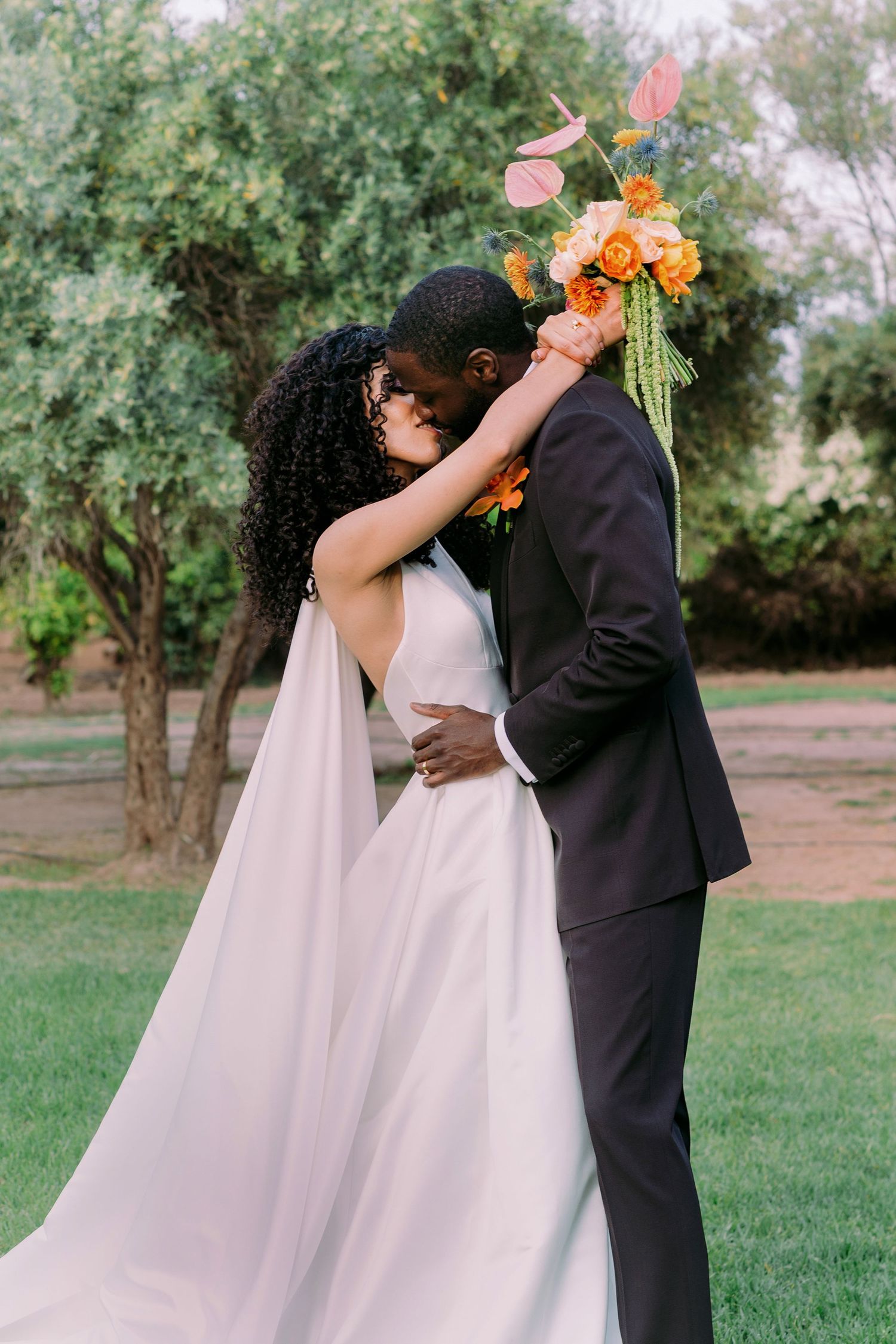 A romantic moment captured between newlyweds with orange floral bouquet in a garden setting.
