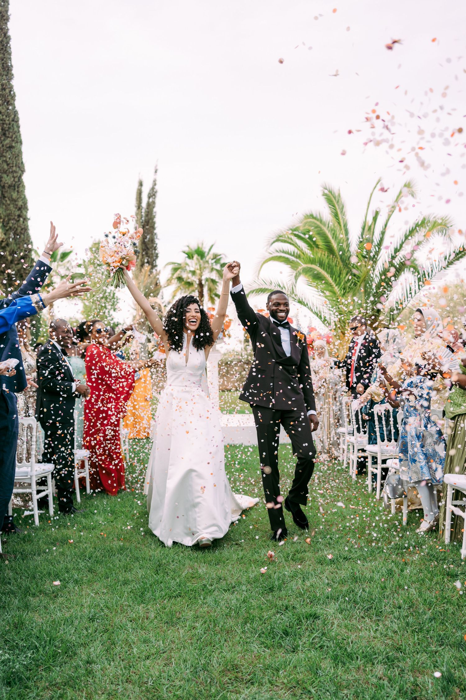 Joyous wedding celebration with red and white confetti being tossed on a lawn.