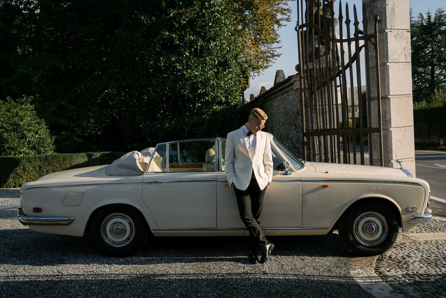 A classic white vintage car parked in front of a stone building on a sunny day.