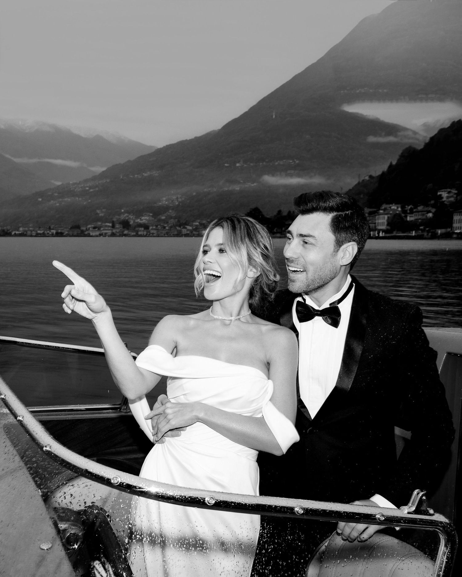 A couple shares a joyful moment while sailing on a lake with mountains in the background.