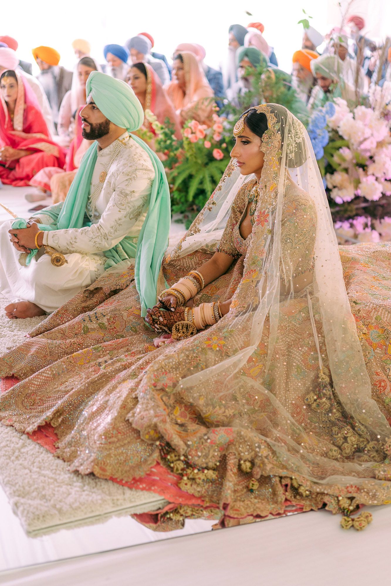 Traditional Sikh wedding ceremony with couple seated on floor wearing ornate mint green and gold ceremonial attire.