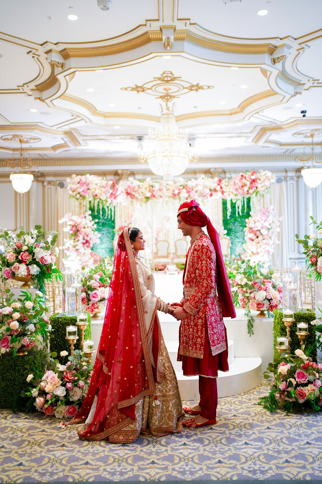 Traditional South Asian wedding ceremony in an elegant ballroom with ornate floral decorations and crystal chandeliers.
