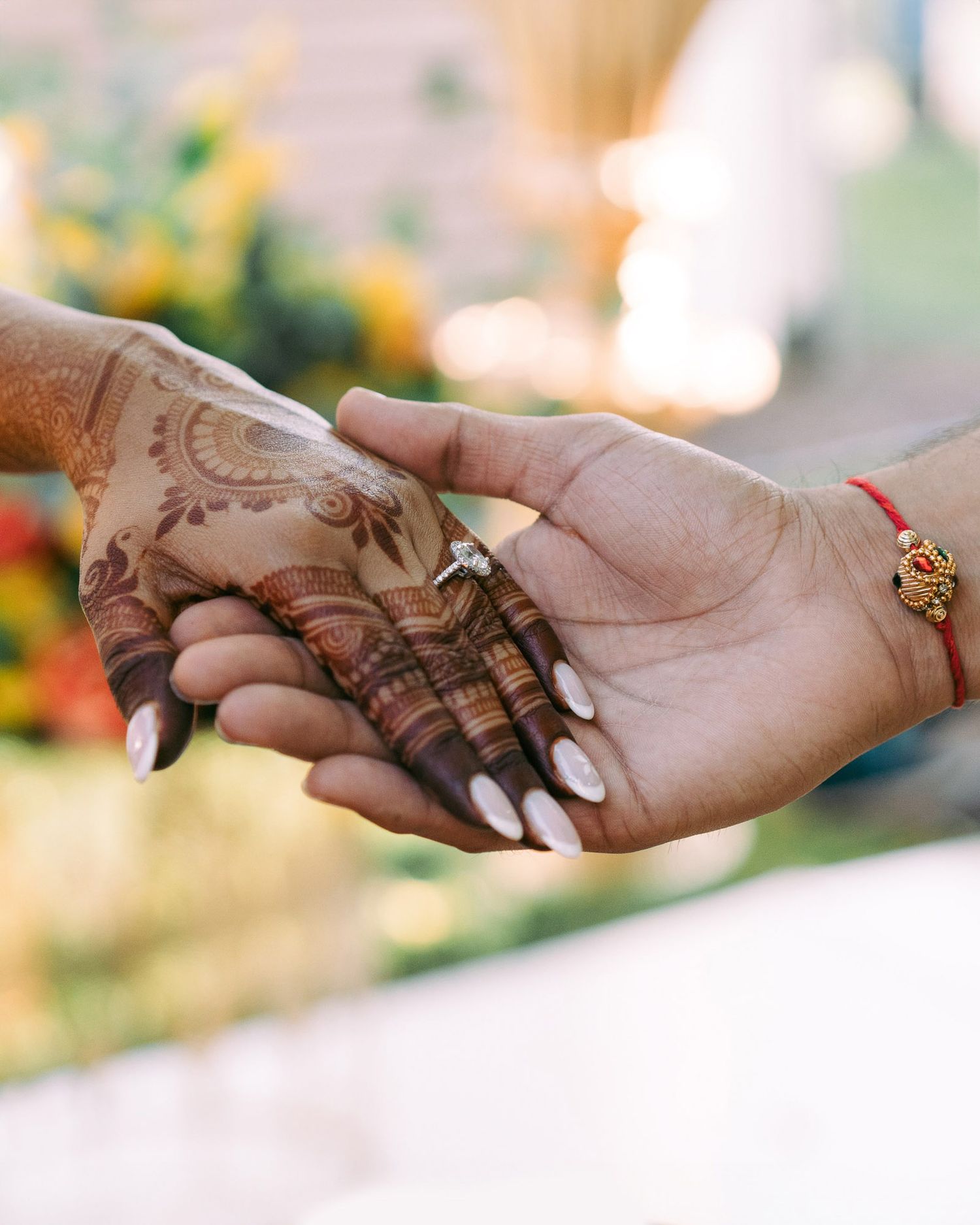 Close-up view of intricate henna designs on hands with gold jewelry and white nail polish.