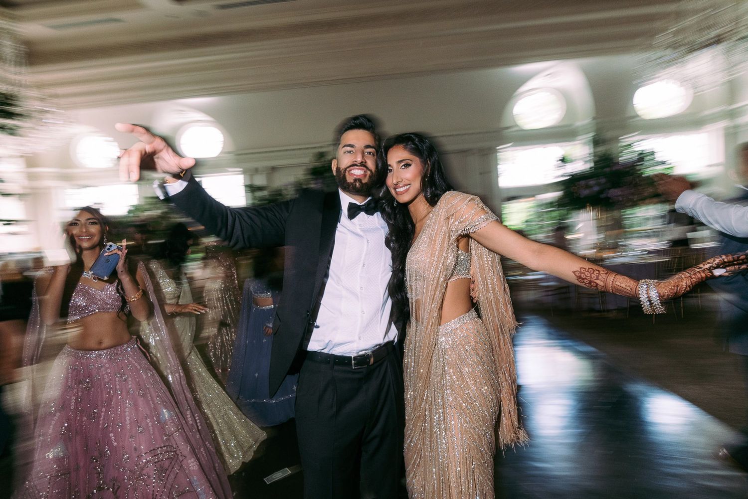 A couple dances joyfully at an elegant indoor reception venue with motion blur and festive lighting.