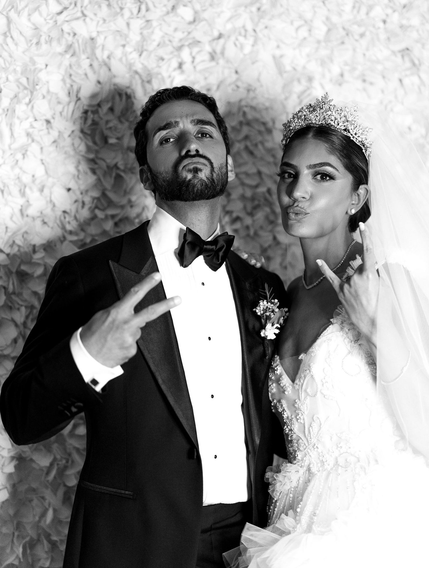 Black and white photo of a bride and groom posing together, with the groom making a peace sign and bride wearing a tiara.