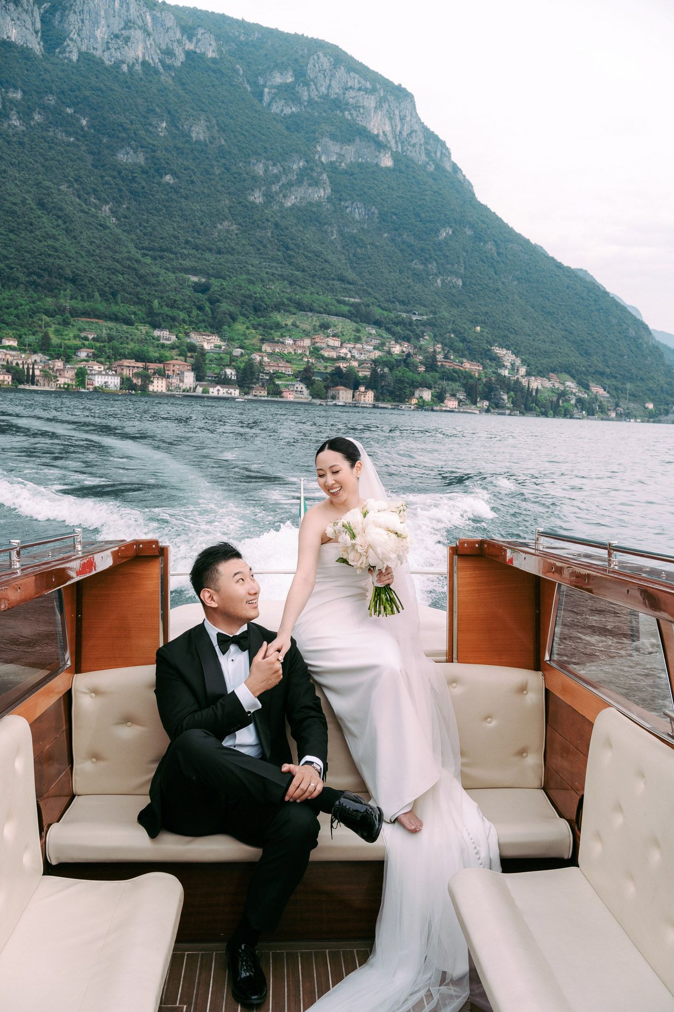 A romantic wedding photoshoot on a boat with a scenic mountain backdrop on Lake Como, Italy.