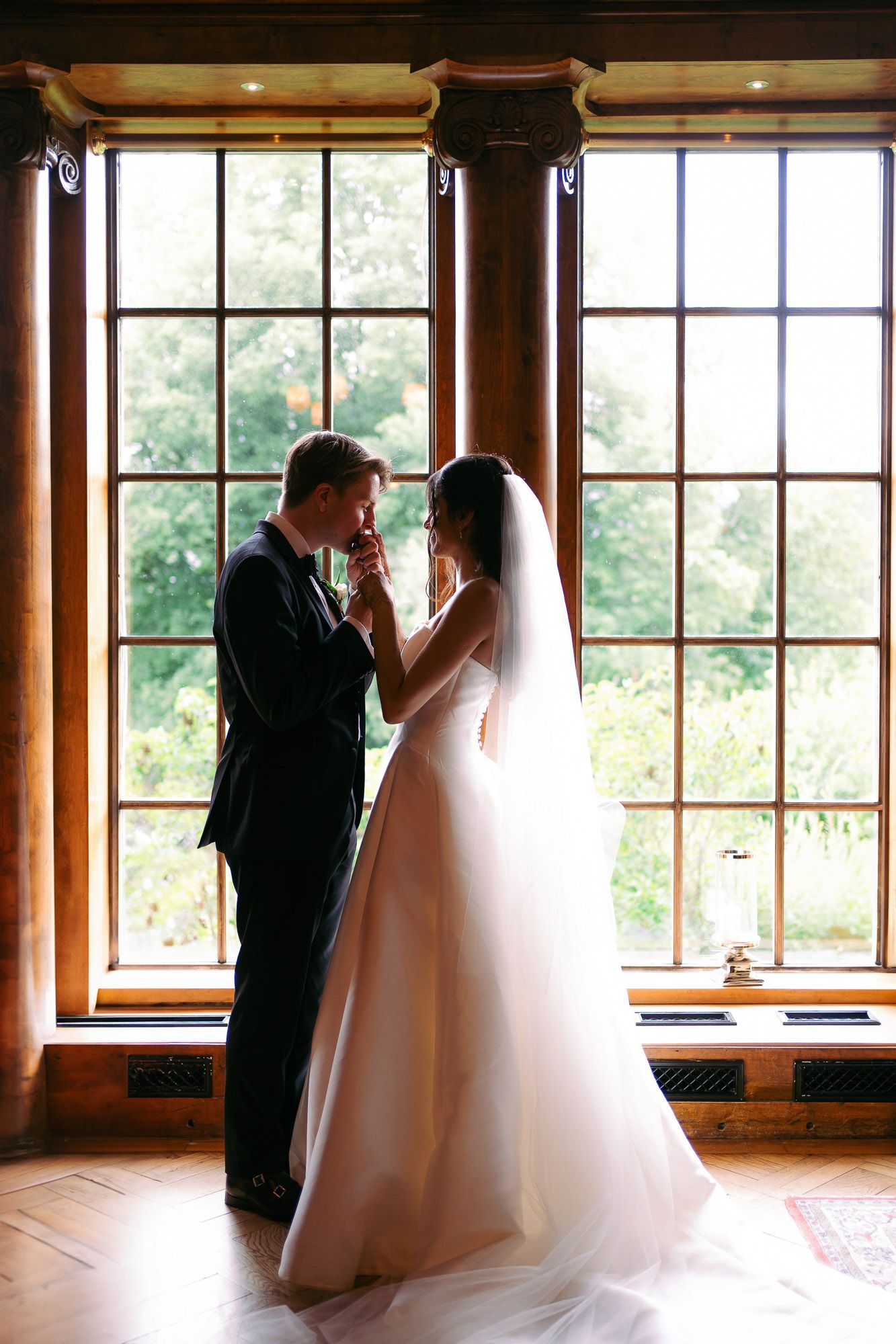 A romantic wedding moment silhouetted against large windows in an elegant venue with natural lighting.
