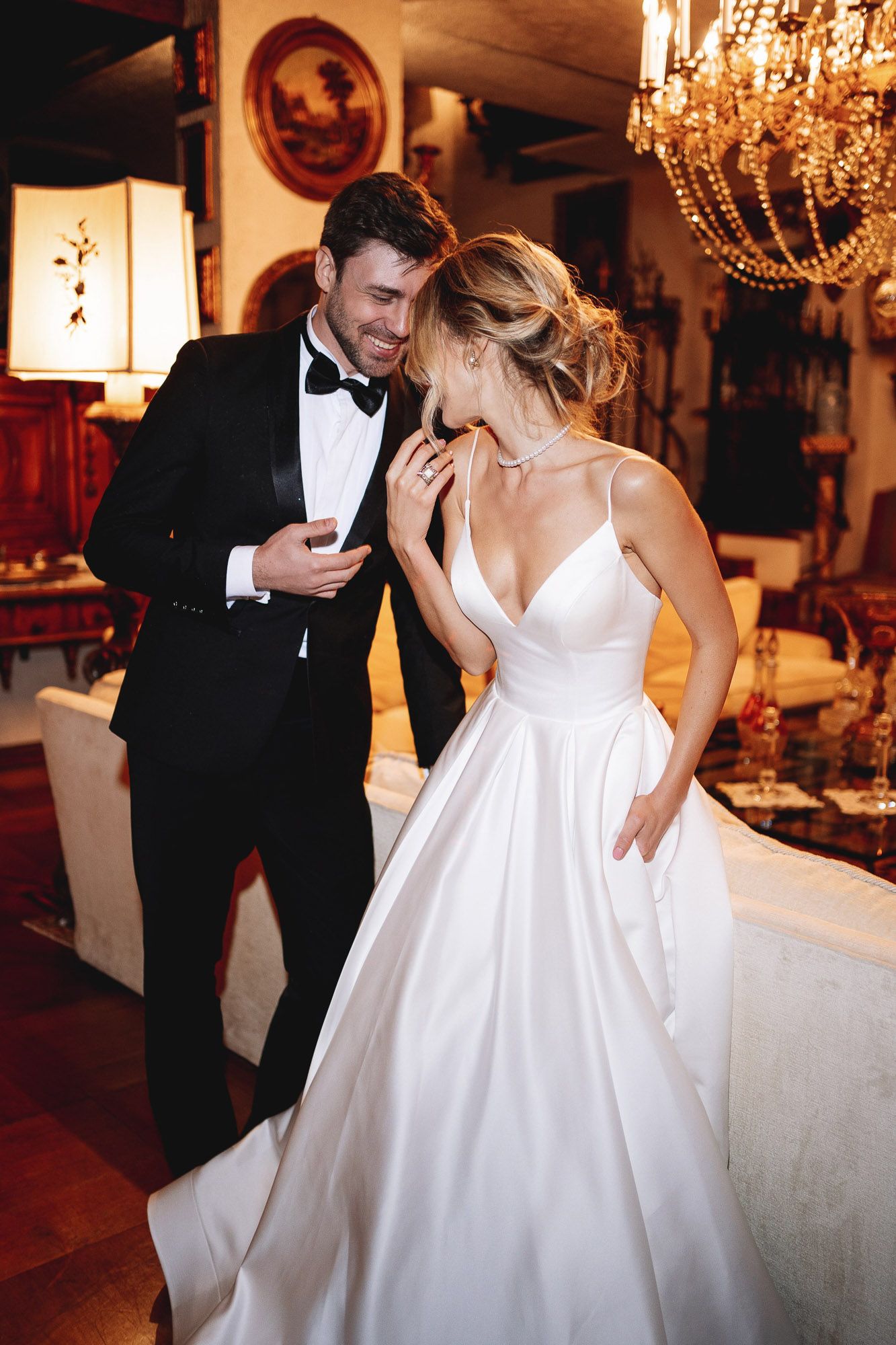 Candid moment between newlyweds sharing a laugh under an elegant chandelier at their wedding reception.