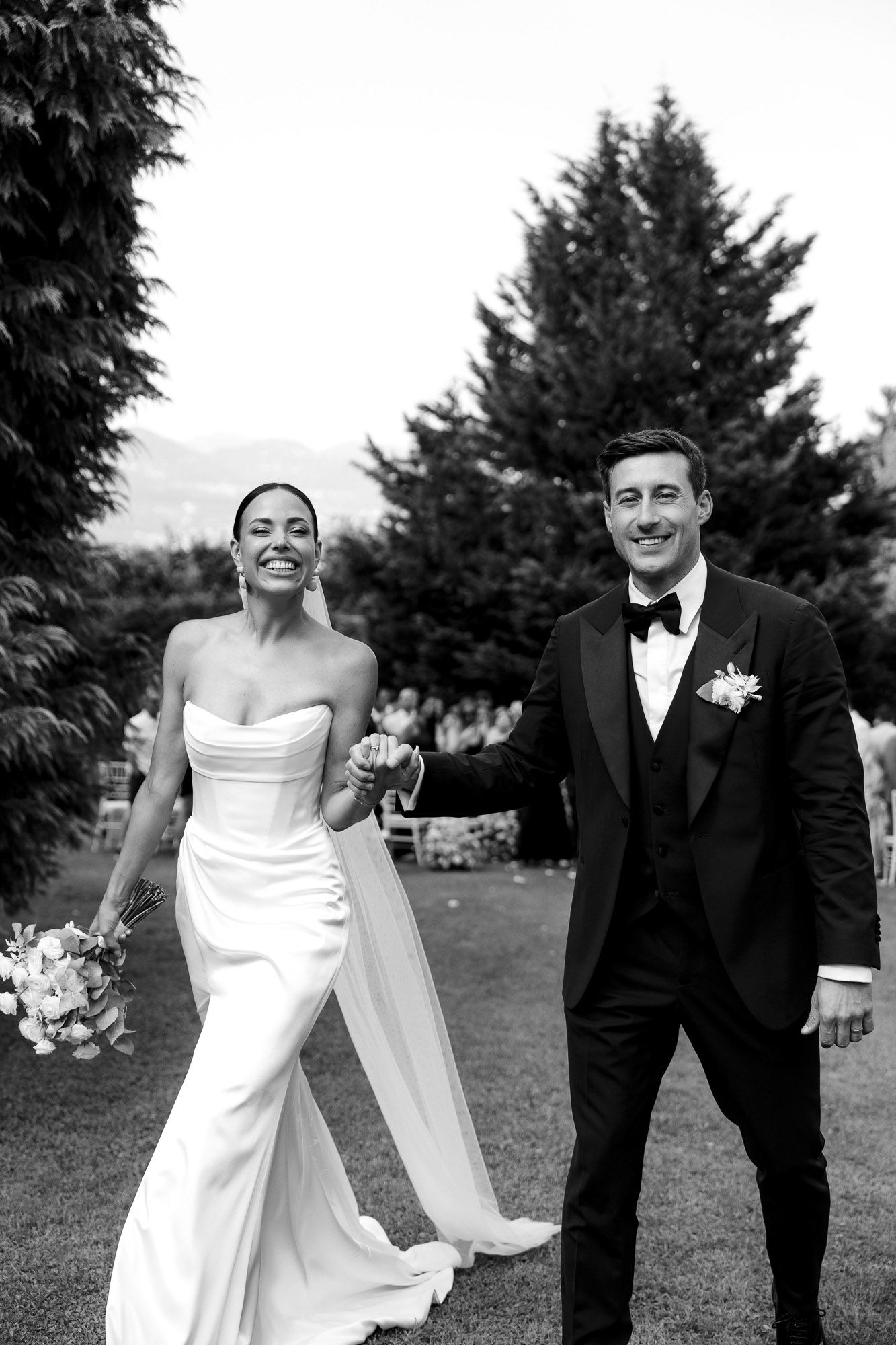 Black and white wedding portraits showing candid moments between newlyweds outdoors with evergreen trees in background.