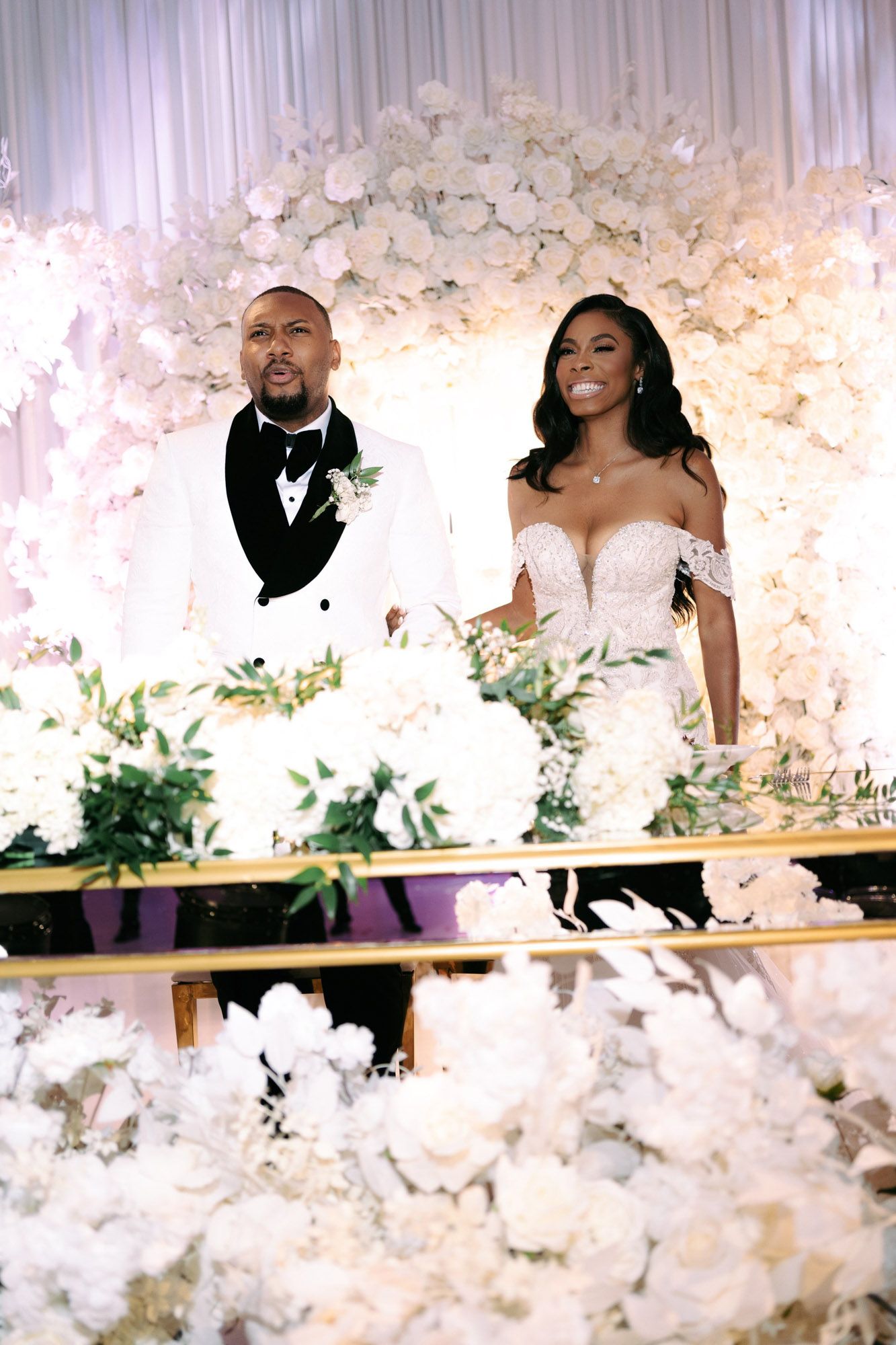 Wedding couple shares intimate moments in front of elegant white floral backdrop during their celebration.