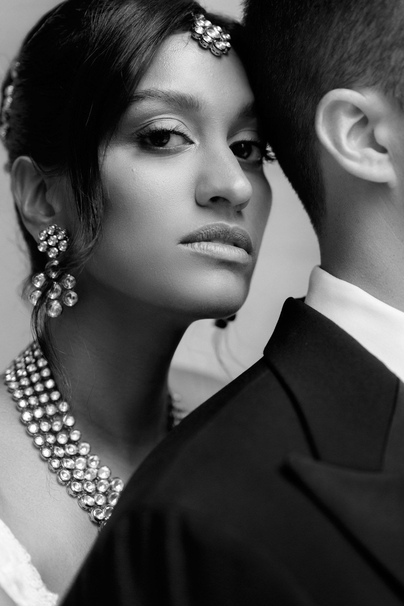 Dramatic black and white fashion portrait showing a glamorous look with statement rhinestone jewelry and elegant styling.