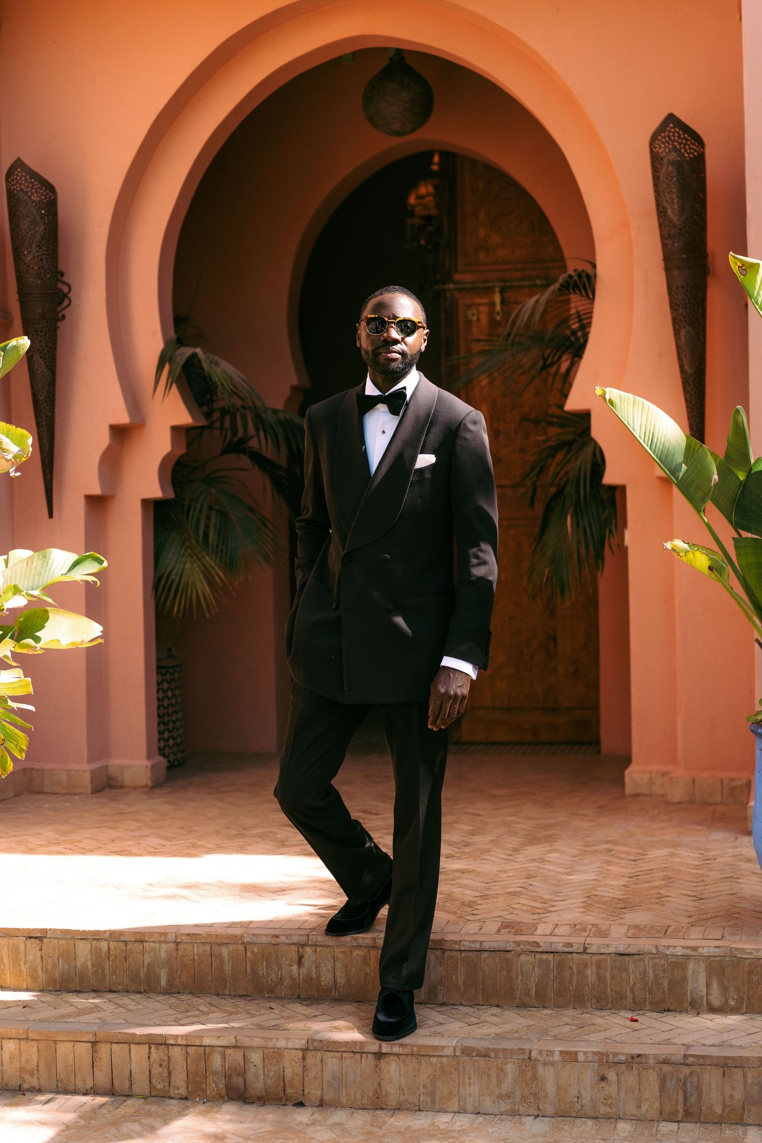 A series of silhouettes in formal attire walking through pink-toned arched hallways.