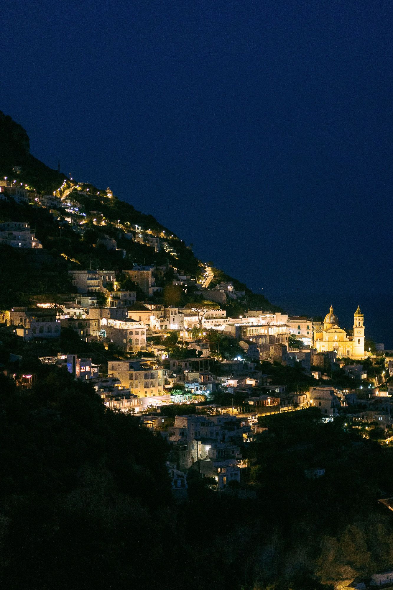 A picturesque hillside village illuminated at night with twinkling lights cascading down the mountainside.