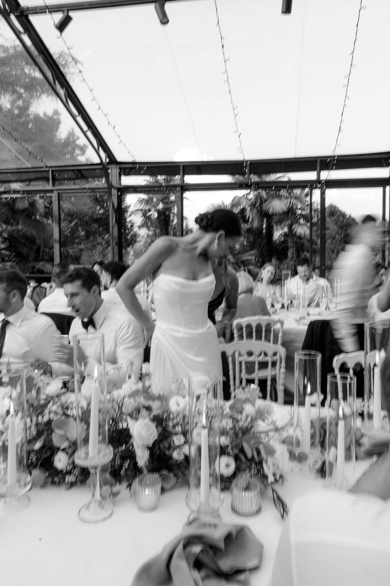 A black and white panoramic sequence of guests dining at tables during an elegant wedding reception under a tent.
