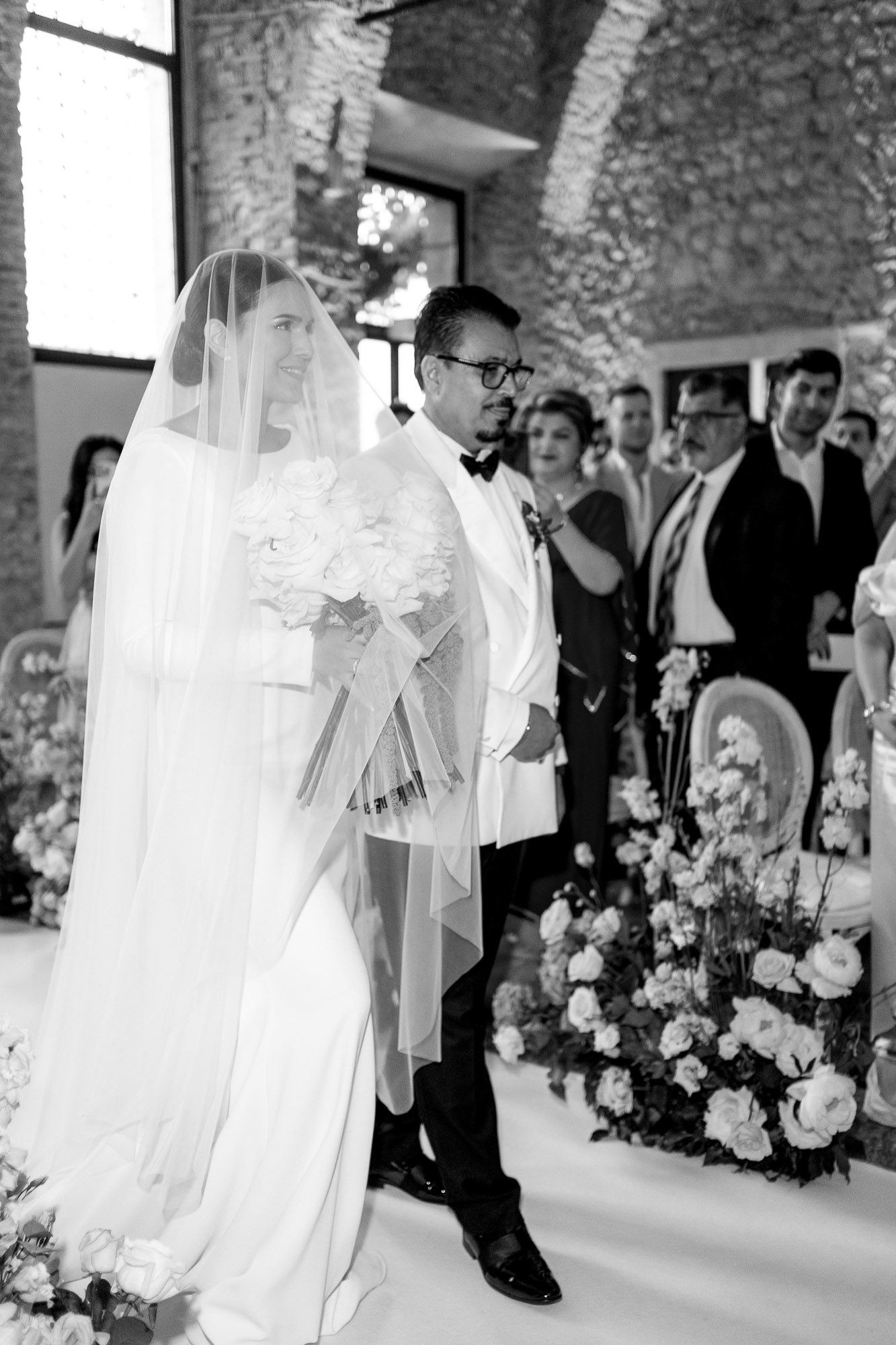 A wedding couple shares a romantic dance moment surrounded by floral arrangements and guests at an elegant venue.