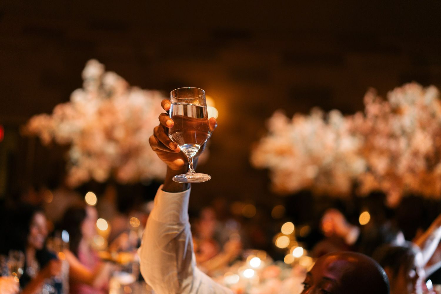 Wedding guests dancing and celebrating on a dark dance floor illuminated by warm glowing lights and decorations.