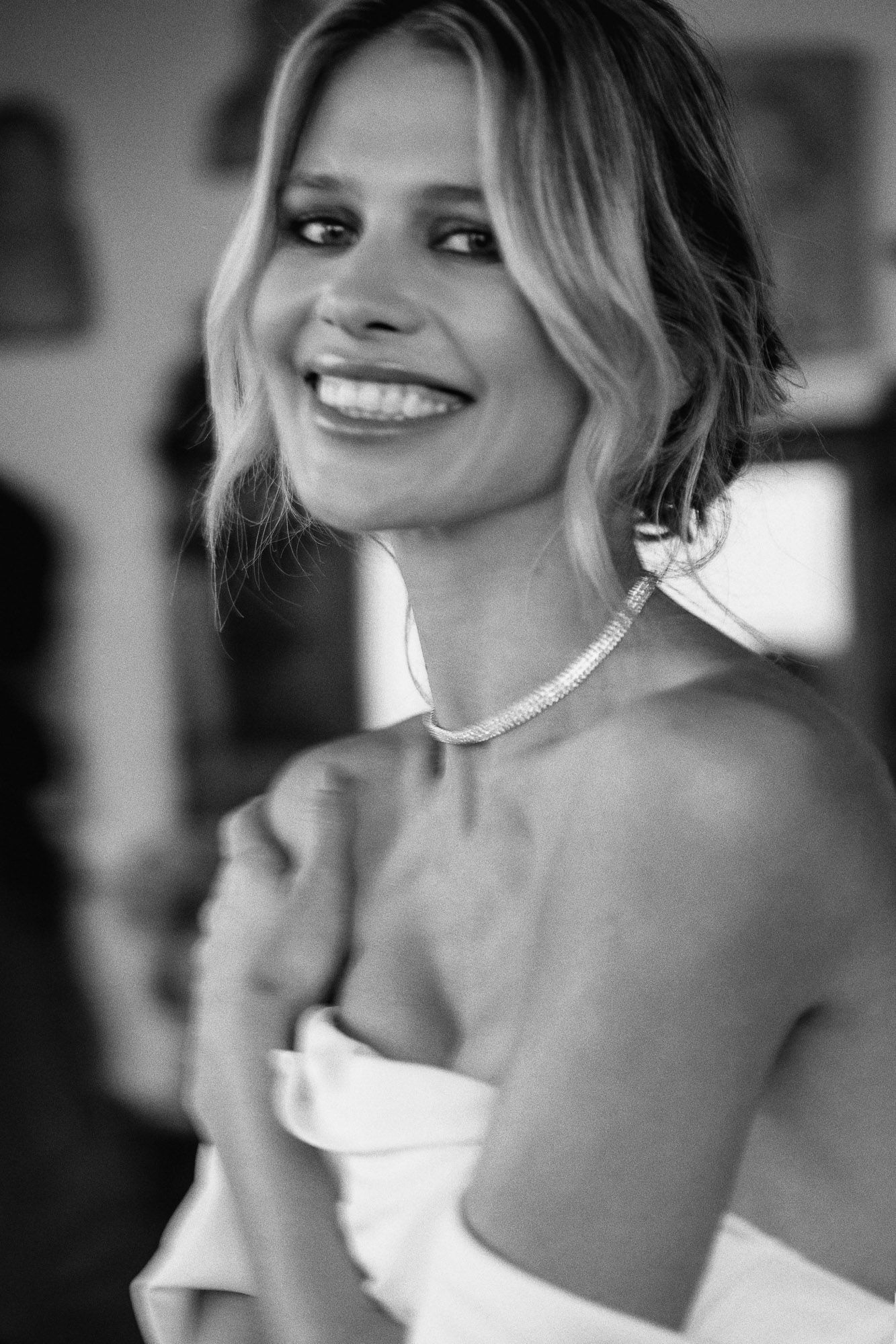 Black and white portrait of someone wearing a strapless dress and pearl necklace with a radiant smile.