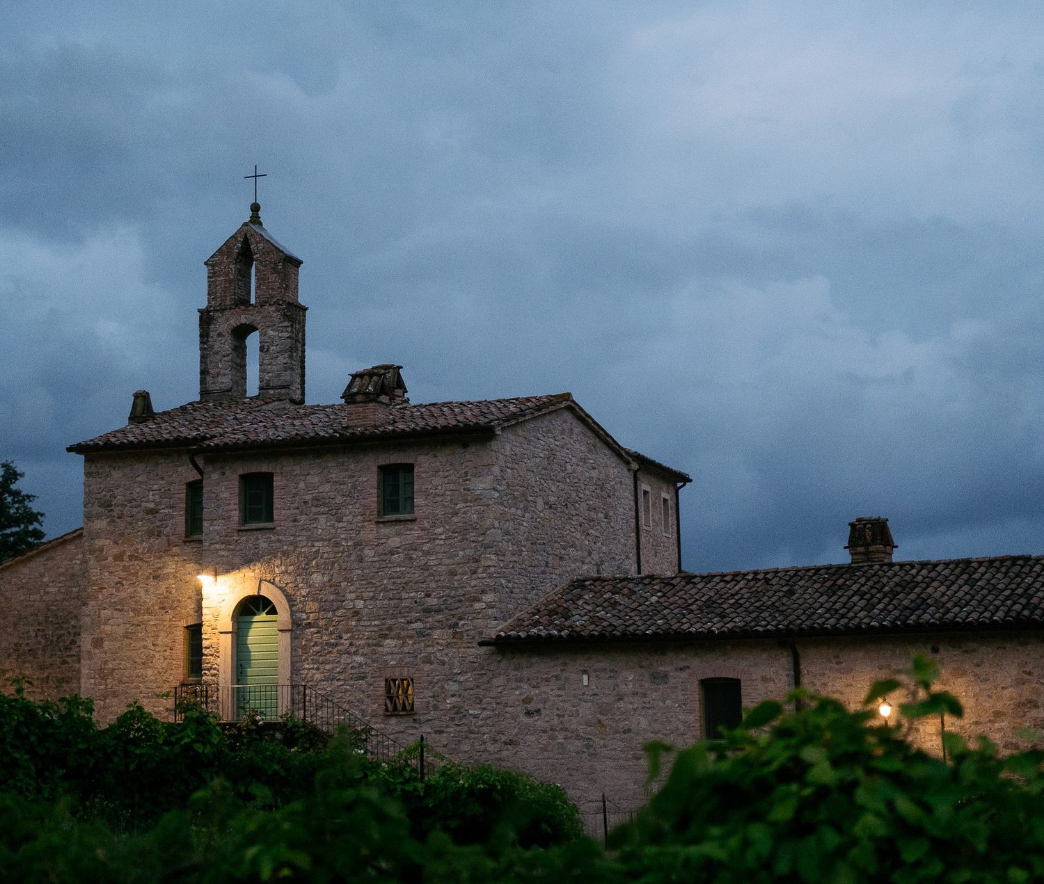 Ancient stone church buildings with bell towers stand against a moody cloudy sky at dusk.