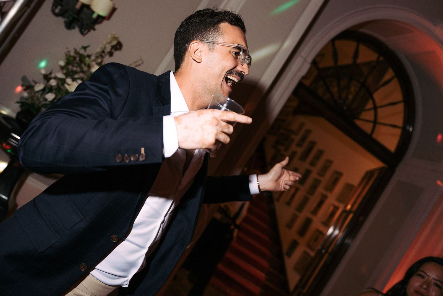 A person in a dark suit and white shirt gestures expressively while speaking at a formal event.