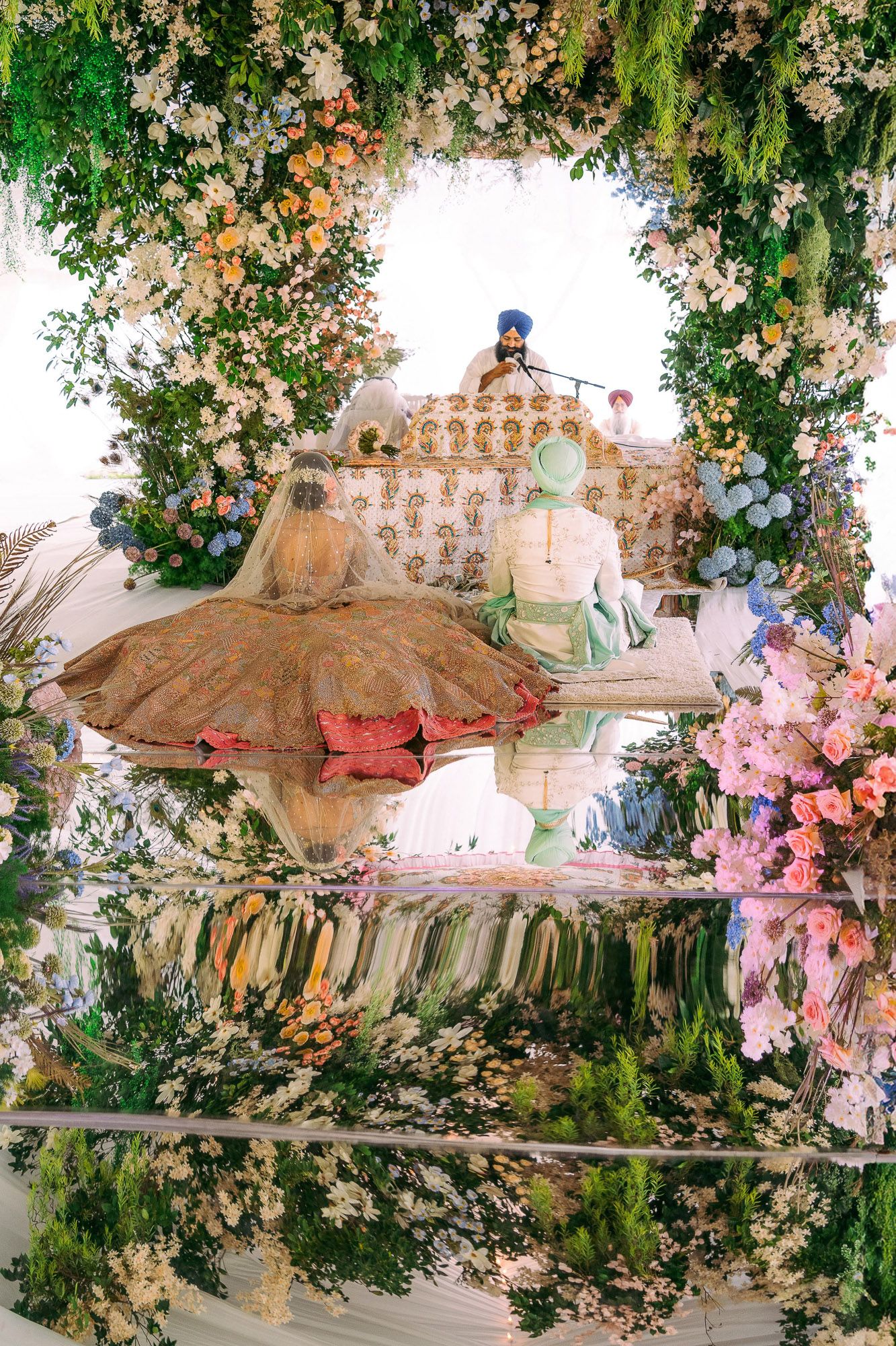 Romantic wedding reception setup with pink floral arrangements and greenery hanging from an ornate white ceiling.