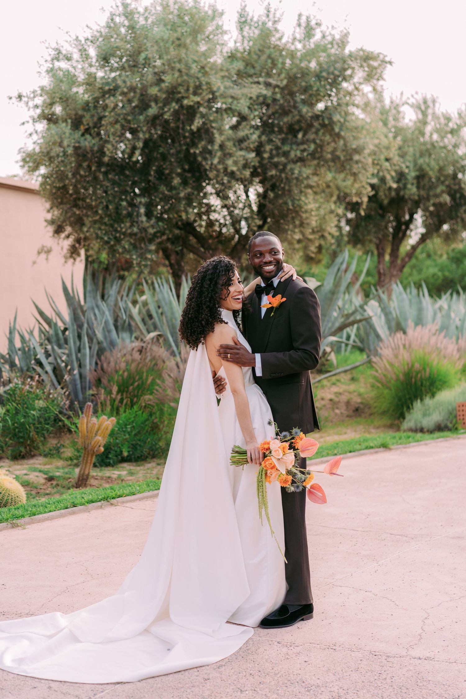 Couple sharing intimate moment during wedding photoshoot in garden setting with desert plants.
