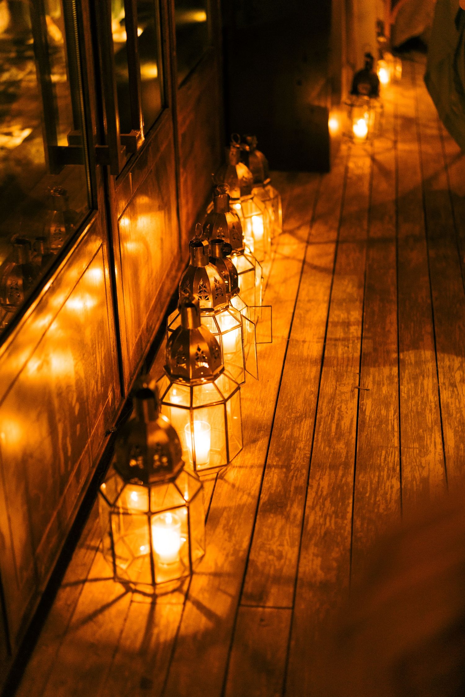 Vintage lanterns cast a warm golden glow across rustic wooden floorboards at dusk.