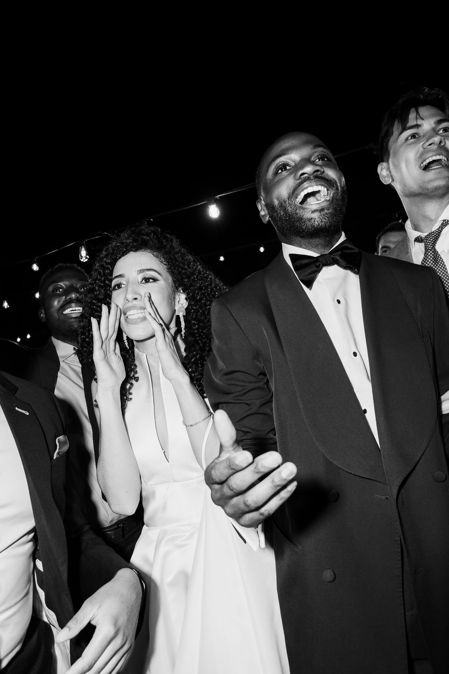 Black and white photo of wedding guests laughing and celebrating at nighttime reception.