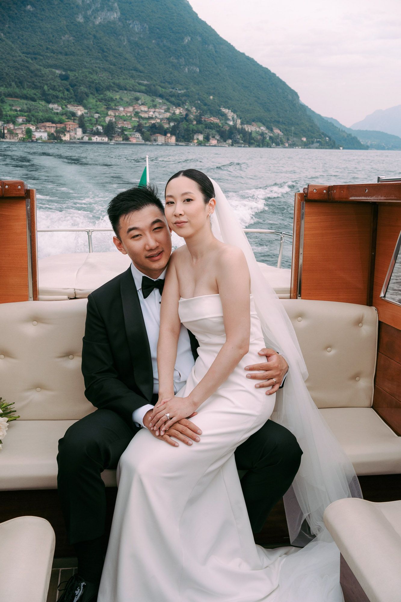 Newlyweds share tender moments during their boat wedding photoshoot against mountainous lakeside scenery.