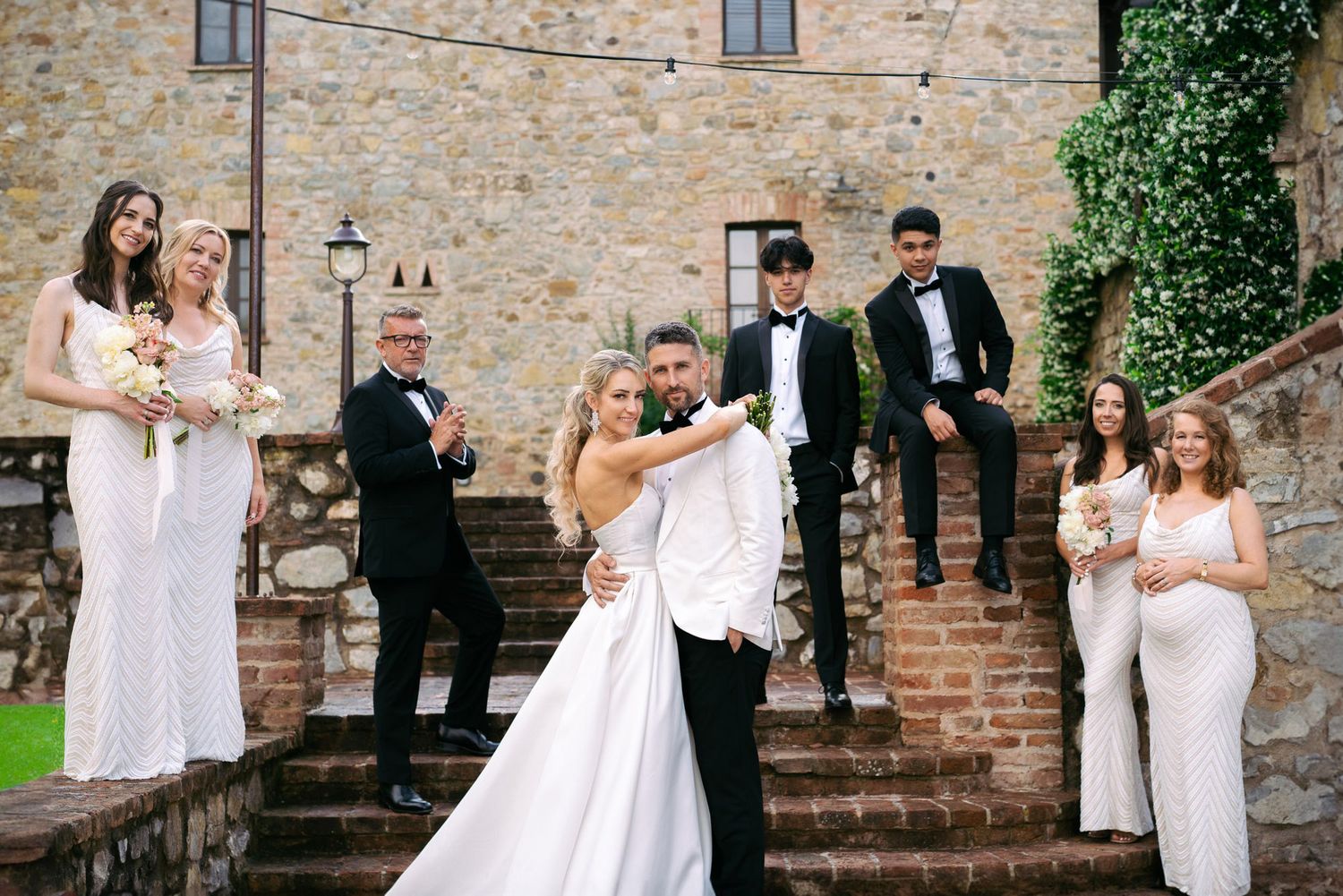 A wedding couple poses for romantic photos against a rustic brick wall and garden setting.