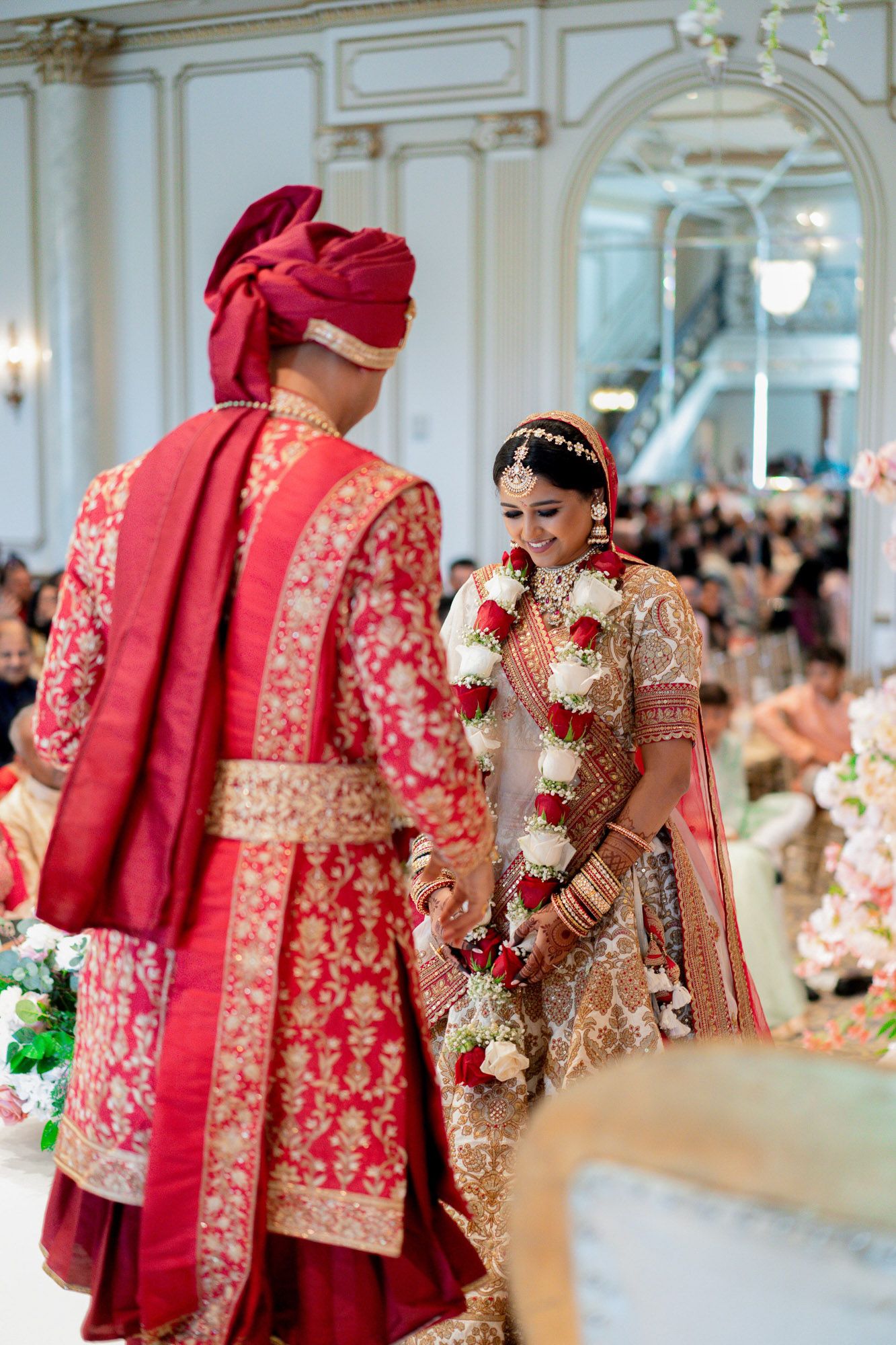 A row of traditional red and gold Indian wedding outfits displayed at an elegant venue with ornate decor.