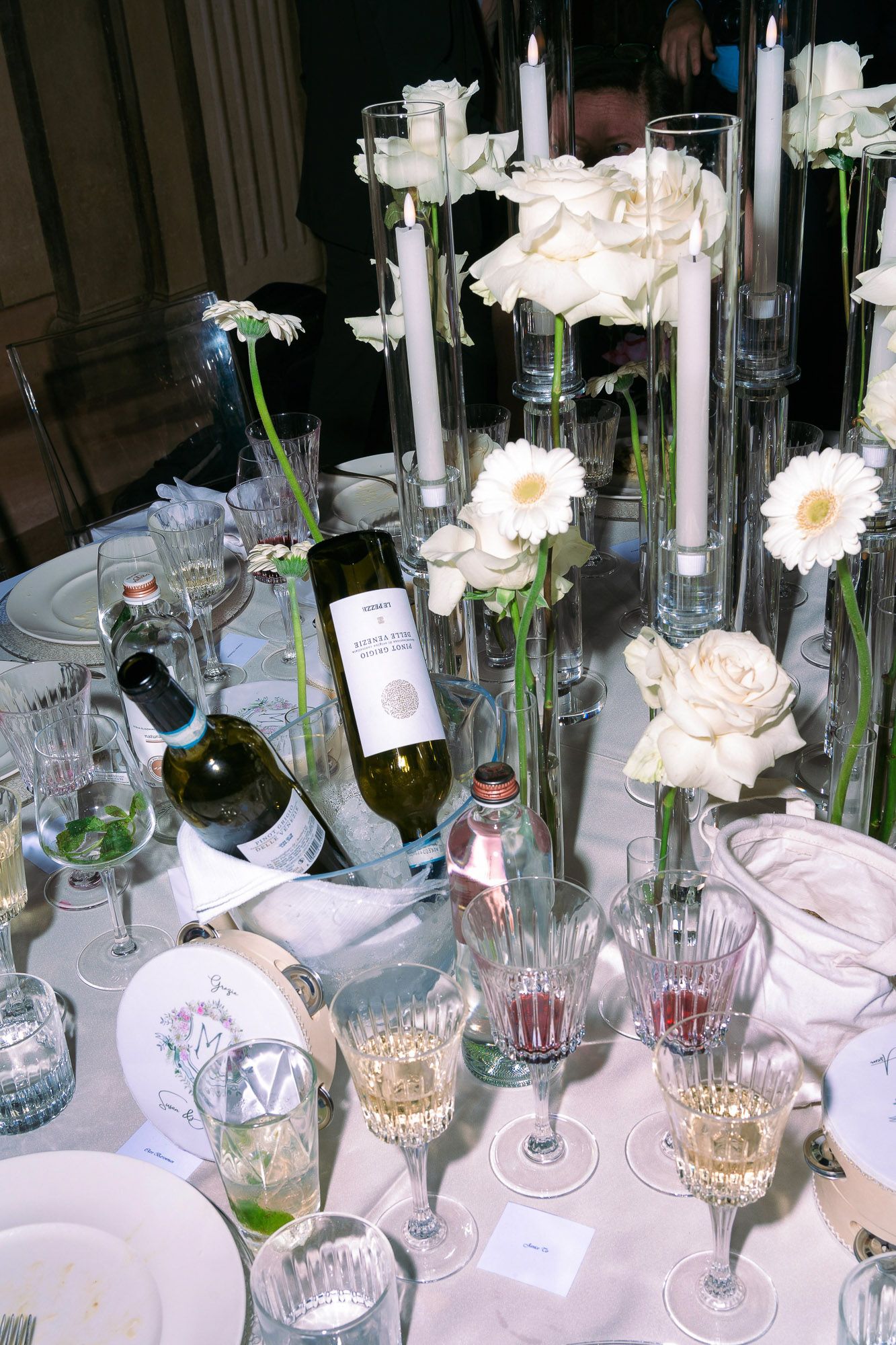 Elegant table setting with white flowers, crystal glasses and wine bottles arranged for a formal dining event.