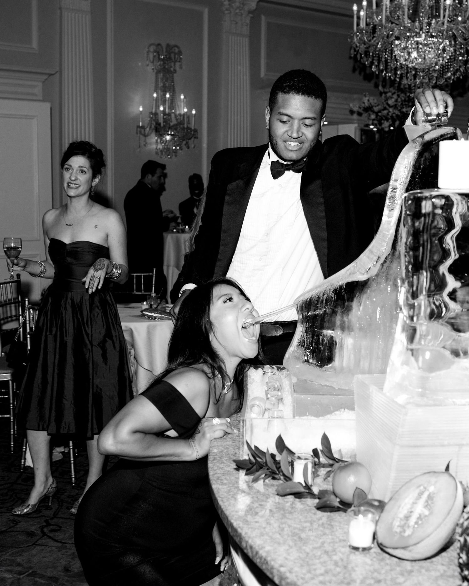 A vintage black and white photo showing people at an elegant formal event with a champagne fountain and crystal chandelier.