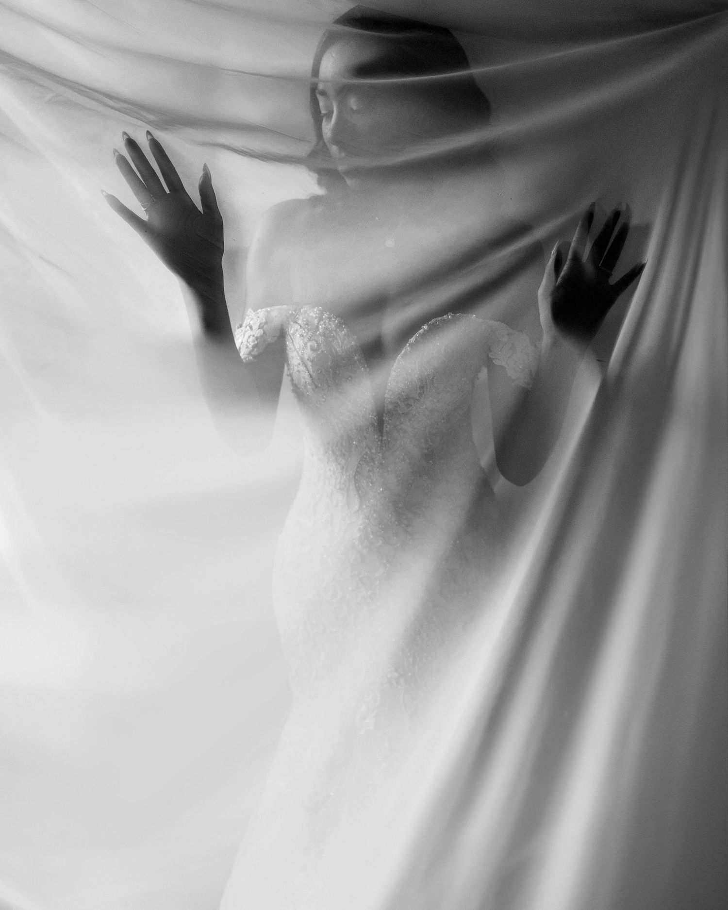 A series of hands pressing against a white fabric backdrop creating dramatic silhouettes and shadows.