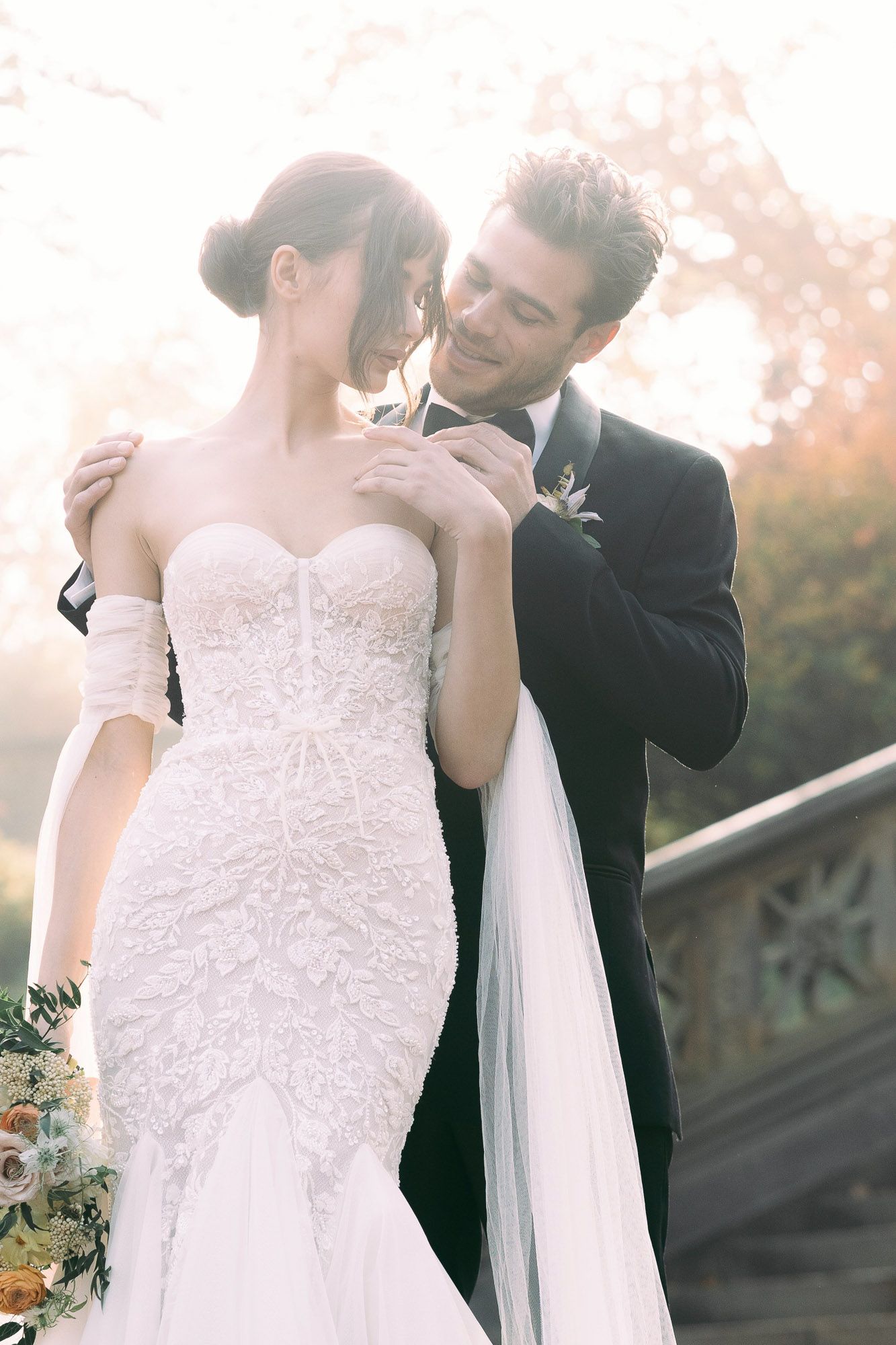 A romantic wedding couple embraces on stone steps during sunset with soft autumn lighting and flowing white veil.