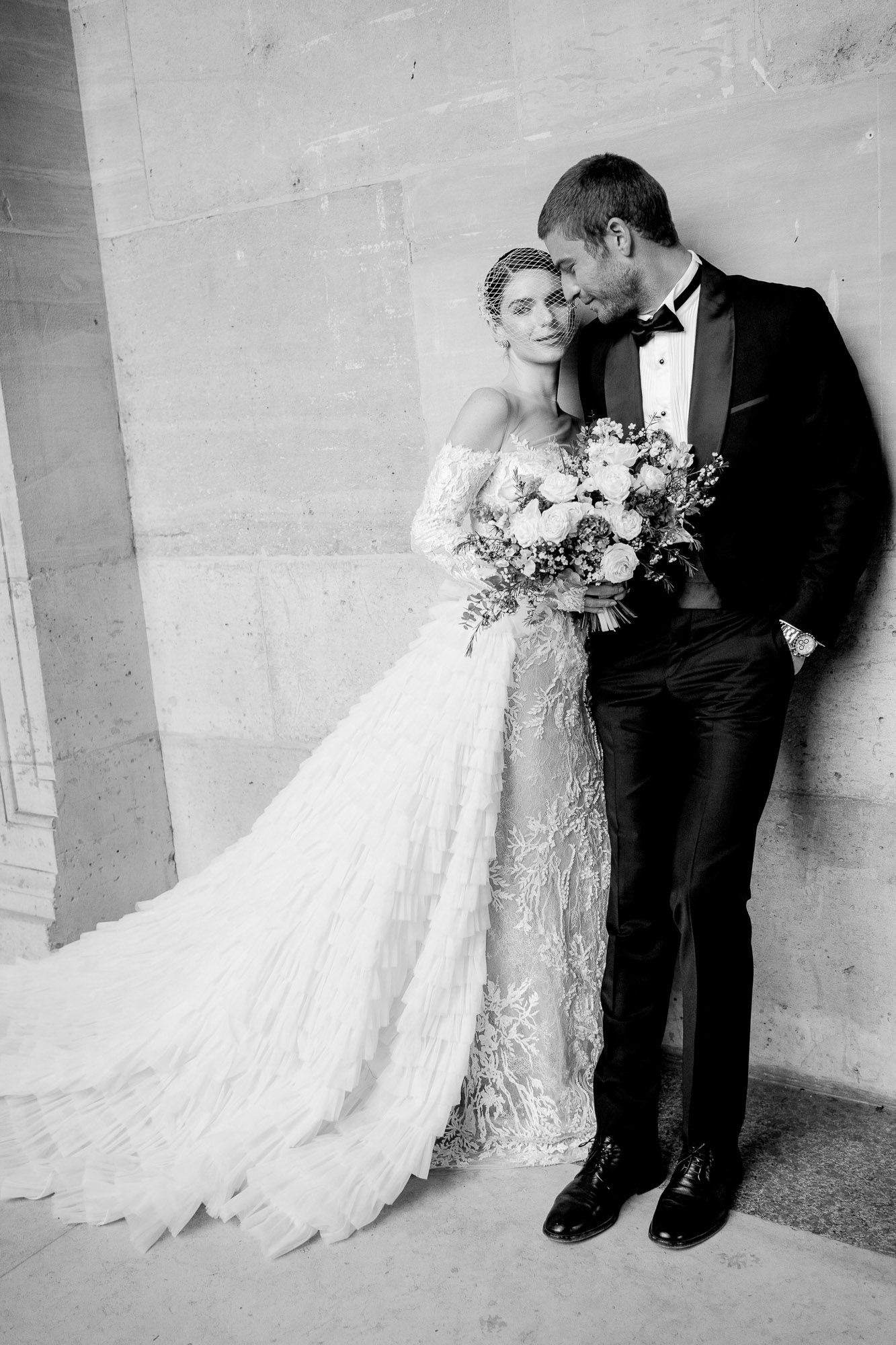 A romantic black and white wedding photo series showing a bride and groom in intimate poses against a light colored wall.