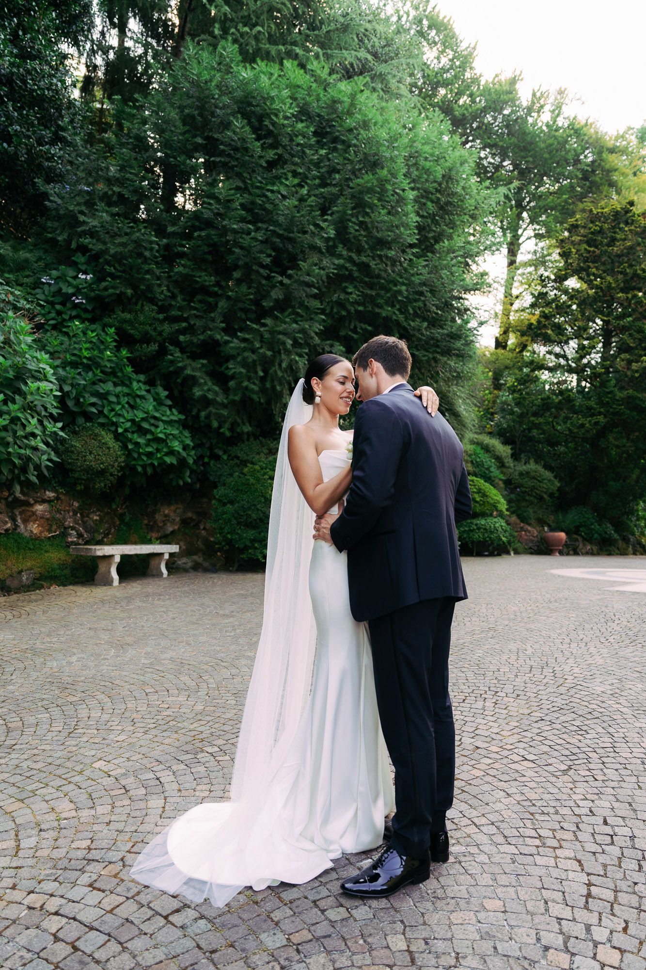 A series of intimate wedding photos on a cobblestone path surrounded by manicured hedges and trees.