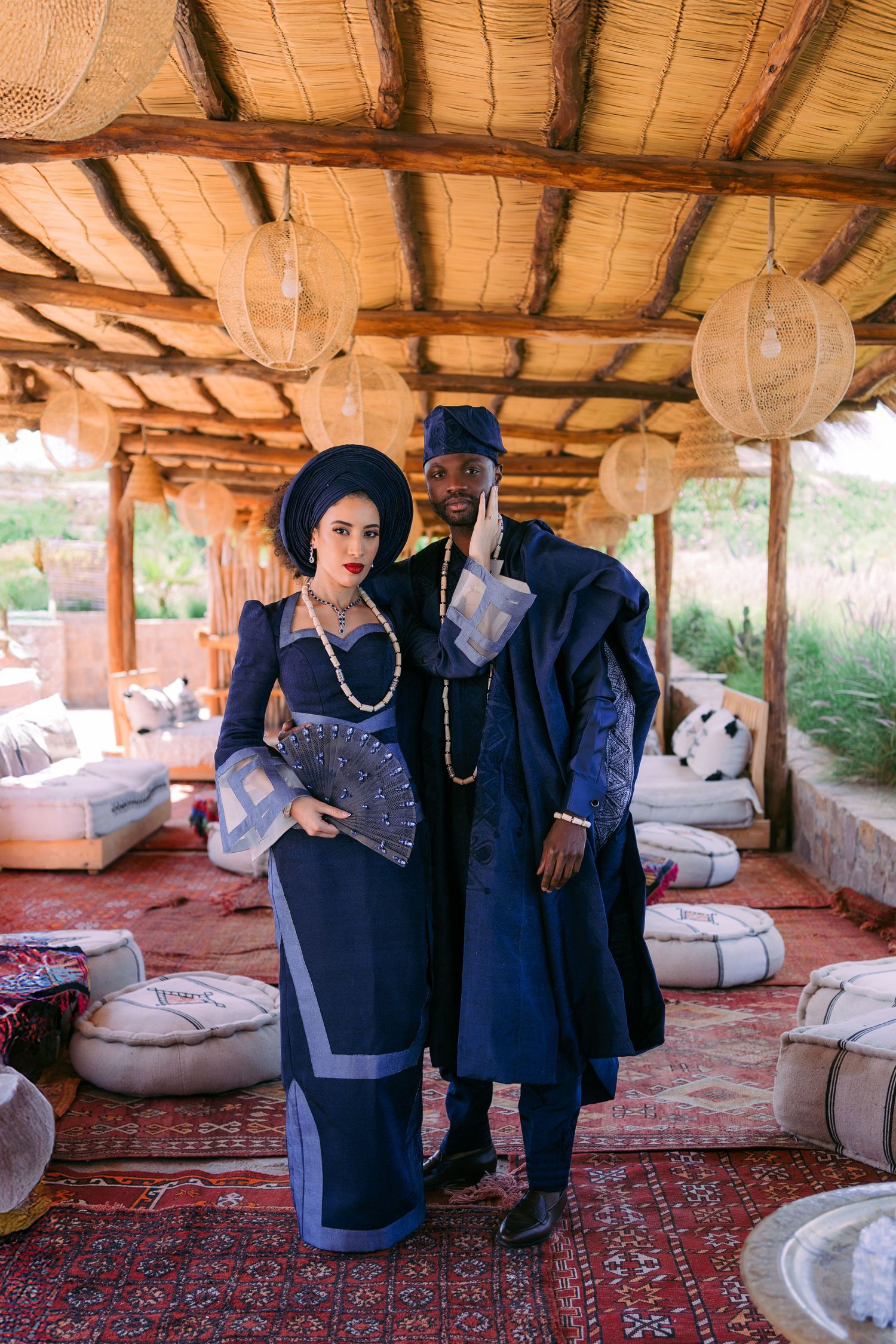 People dressed in formal navy blue outfits socialize in a covered outdoor space with traditional rugs and cushioned seating.