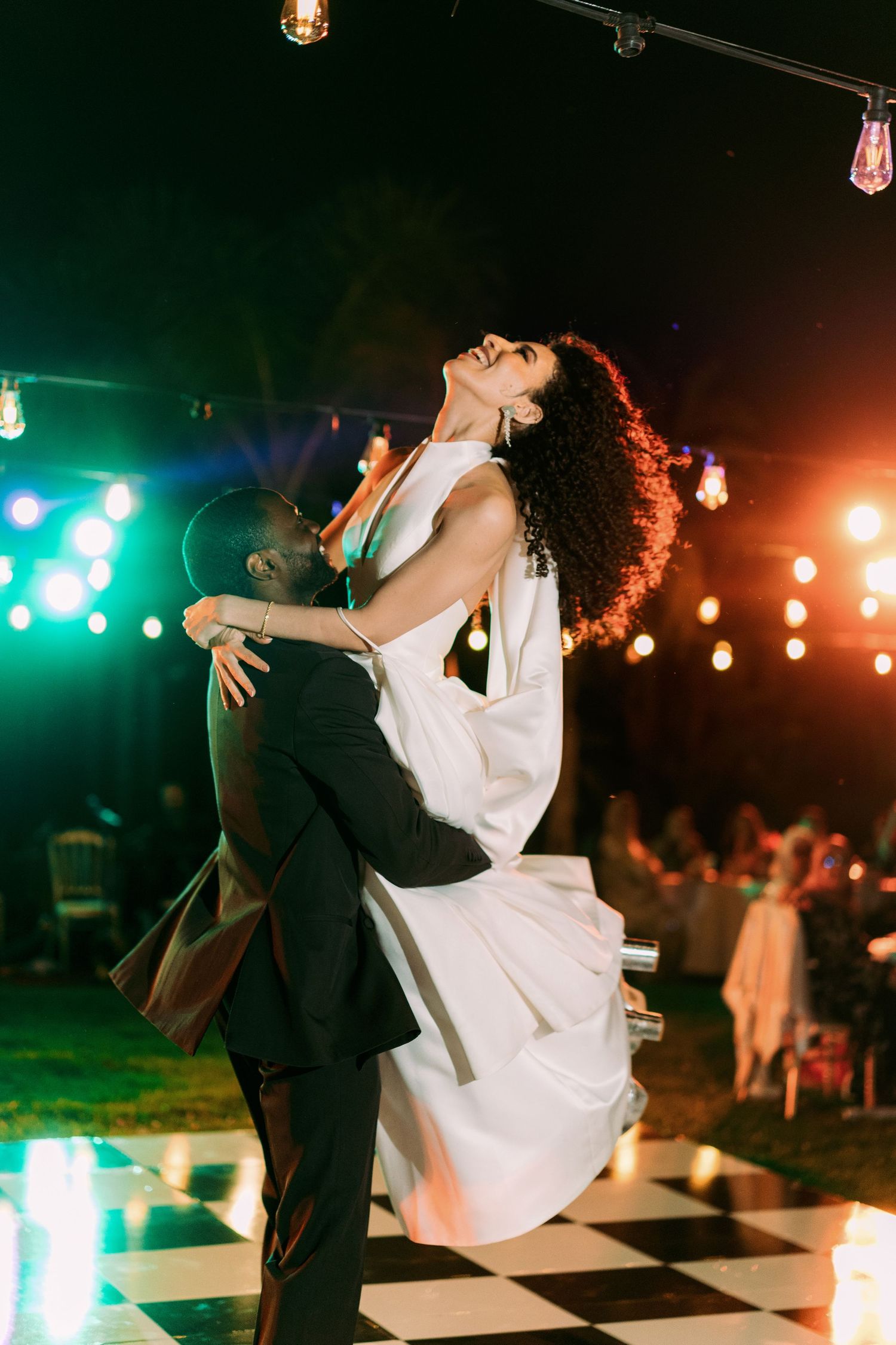 Couples dancing beneath colorful string lights at an outdoor evening celebration.