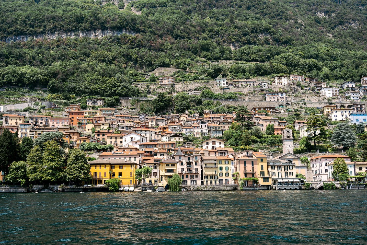 Panoramic view of colorful Italian lakeside village buildings nestled against lush green mountains along Lake Como.