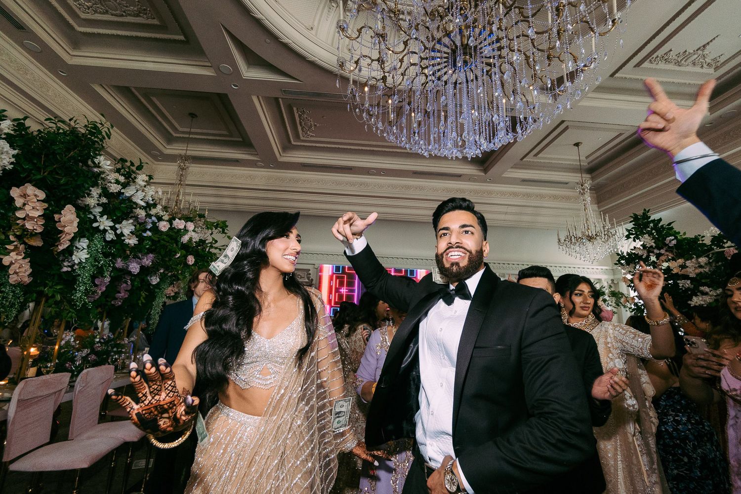 Wedding guests dancing and celebrating on a dance floor under elegant crystal chandeliers at an indoor reception venue.
