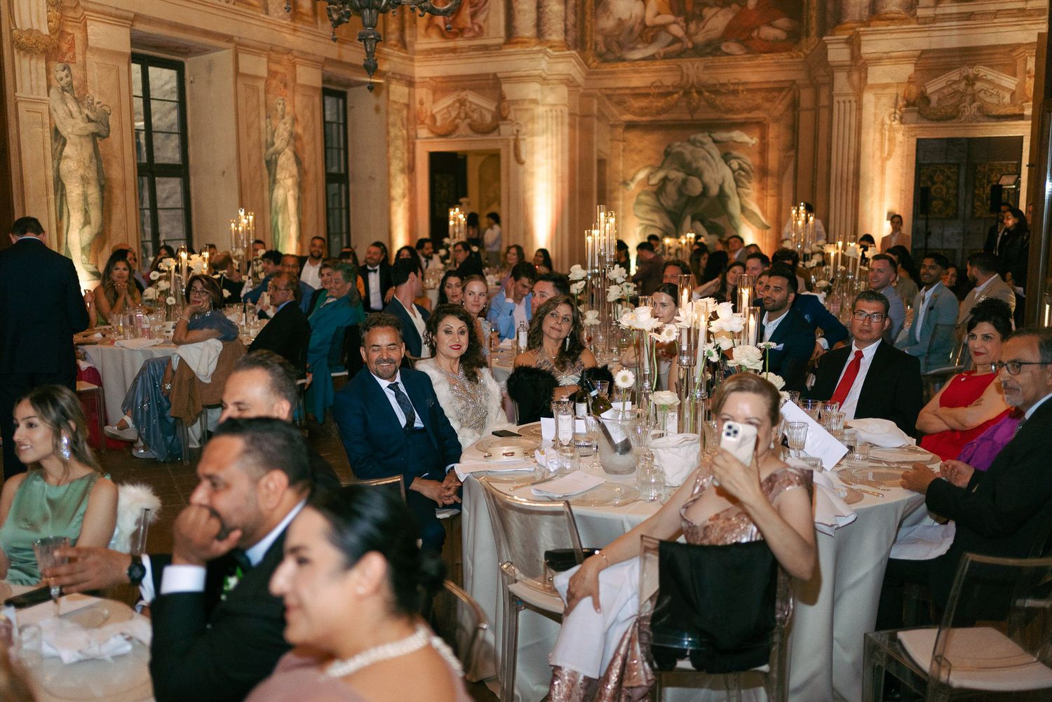 Elegant wedding reception in a grand ballroom with round tables decorated in white linens and floral centerpieces.