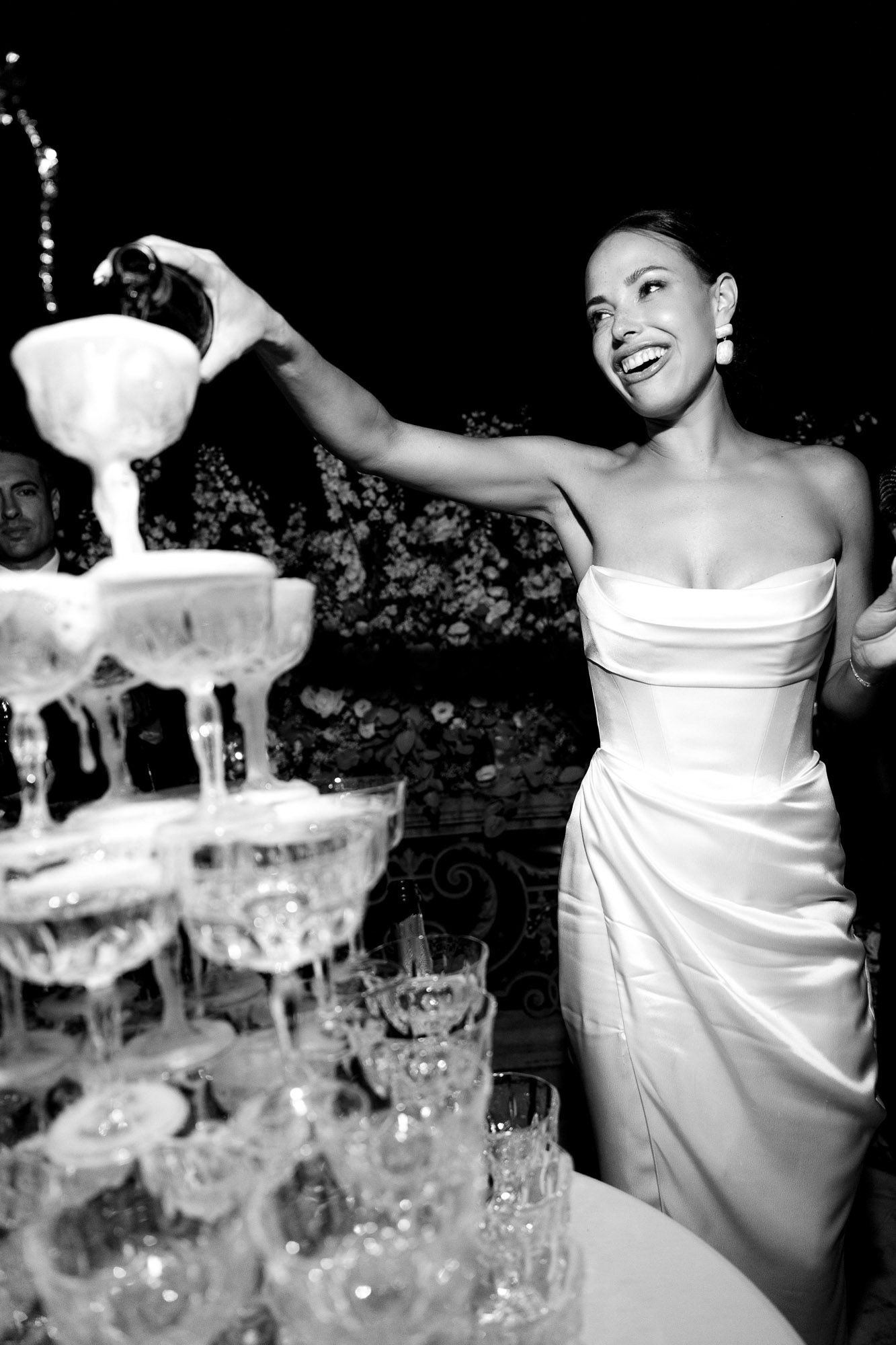 A champagne tower being poured at an elegant celebration with crystal glasses stacked in pyramid formation.