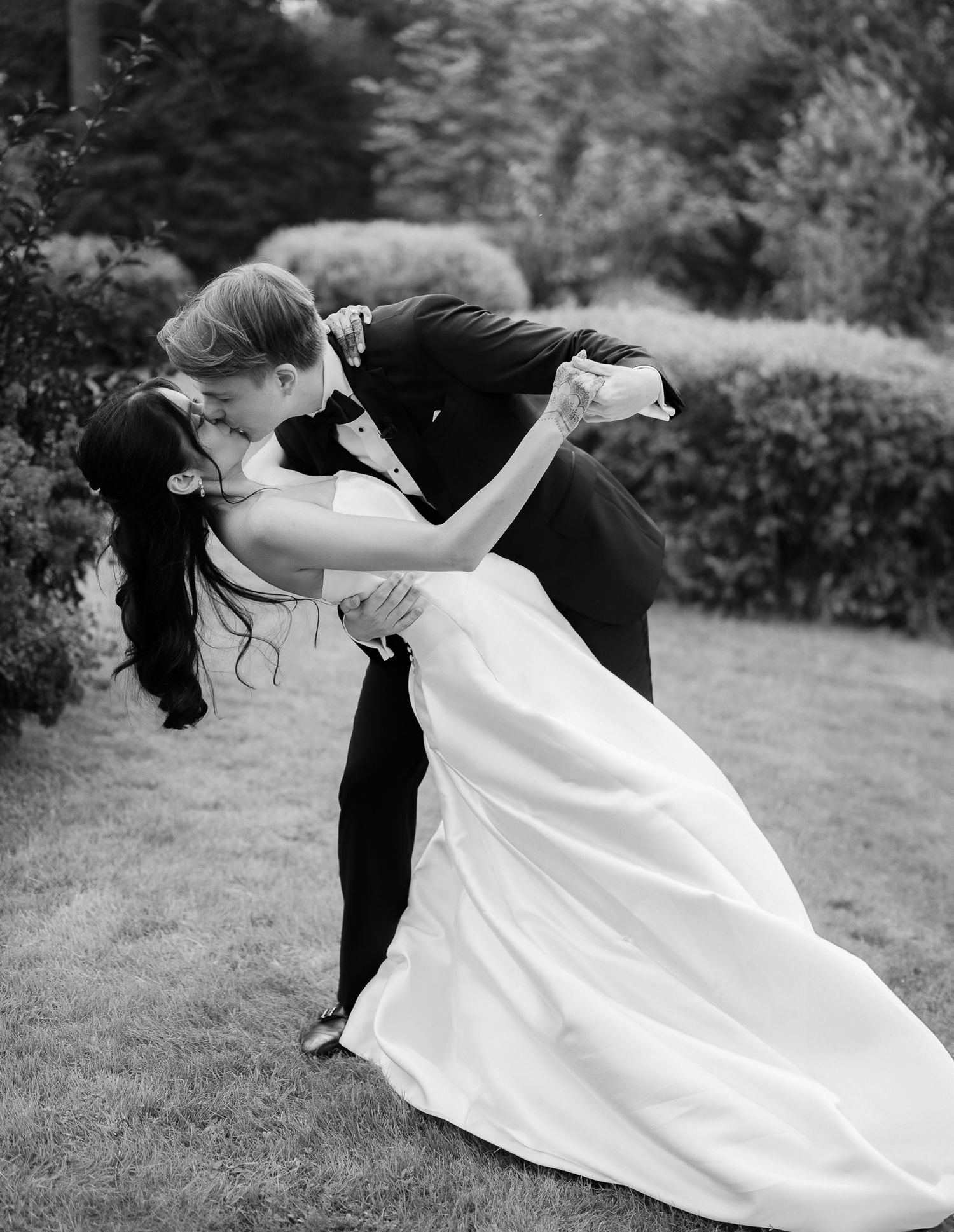 A romantic black and white wedding photo showing a couple in an elegant dip pose on a garden lawn.